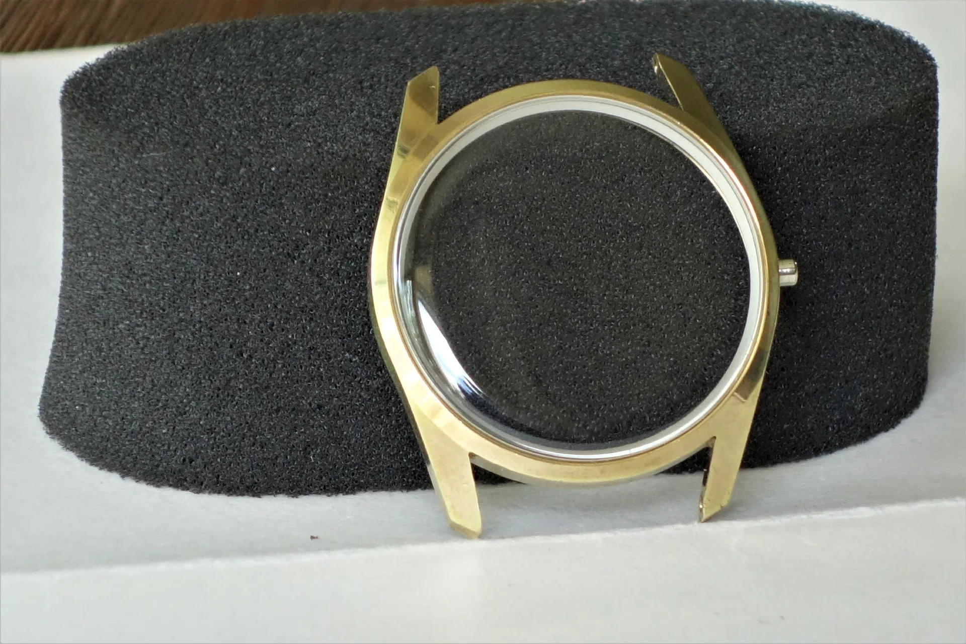 Rundes Uhrgehäuse aus Metall in goldfarbener Optik mit montiertem Uhrglas.