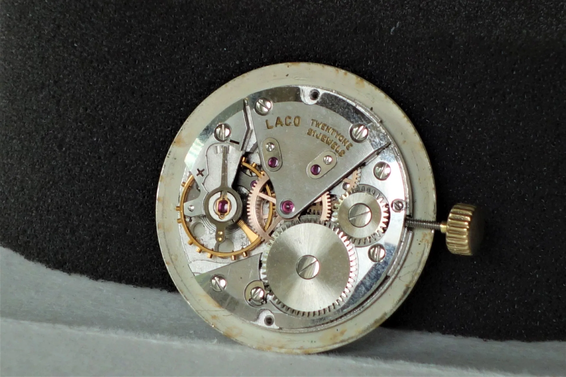 Silberfarbenes mechanisches Uhrwerk mit sichtbaren Zahnrädern und goldfarbener Krone.