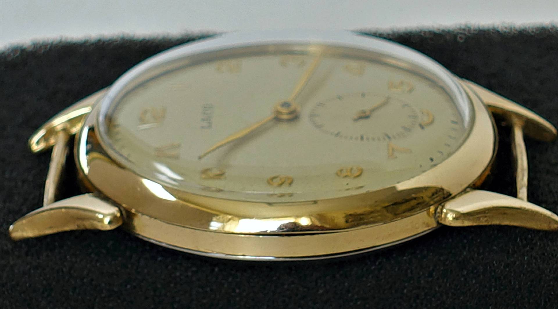 Flache Armbanduhr mit goldfarbenem Gehäuse und hellem Zifferblatt.