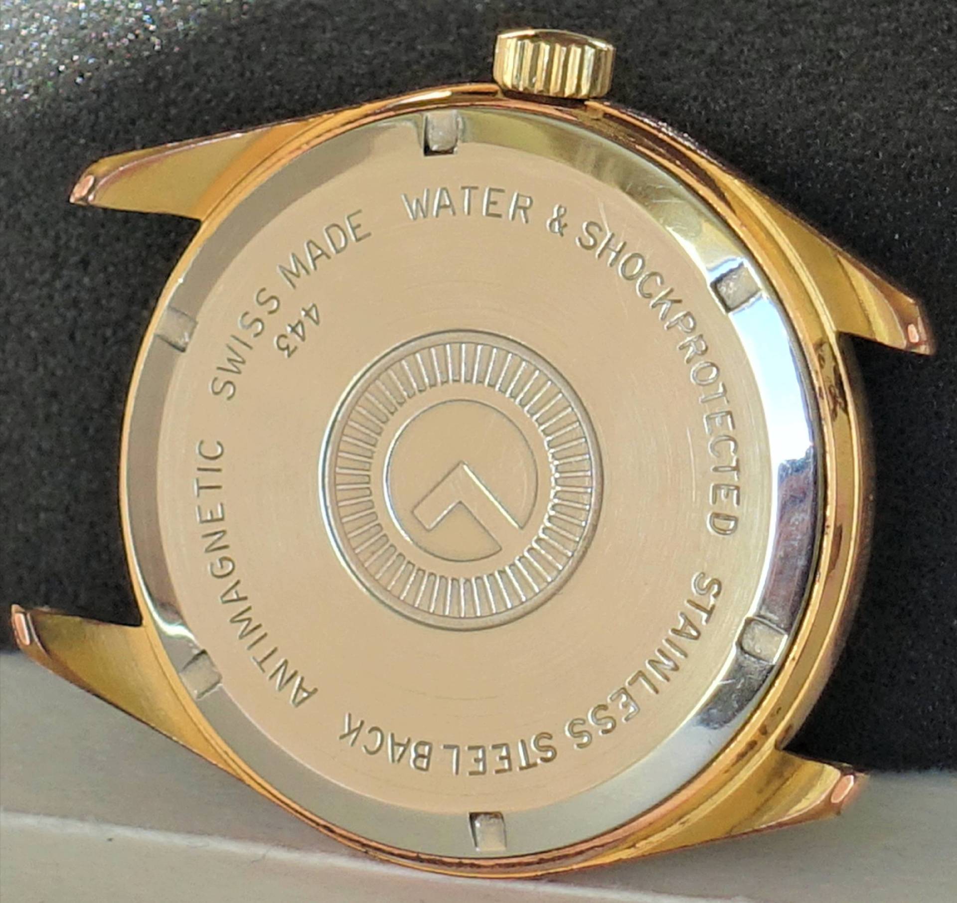 Rundes goldfarbenes Uhrgehäuse mit silberfarbener Rückseite und verschraubtem Boden.