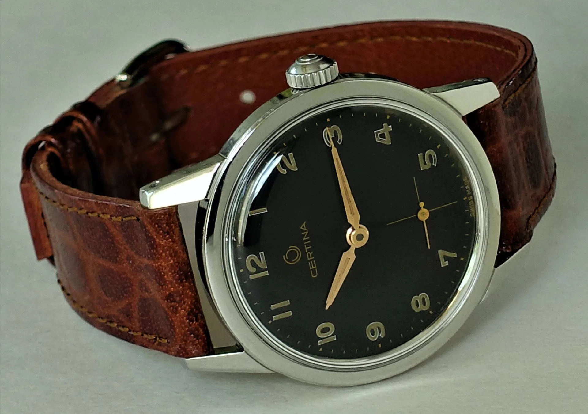 Schwarze Armbanduhr mit braunem Armband und silberfarbenem Gehäuse, Zifferblatt mit goldfarbenen Zeigern und Zahlen.