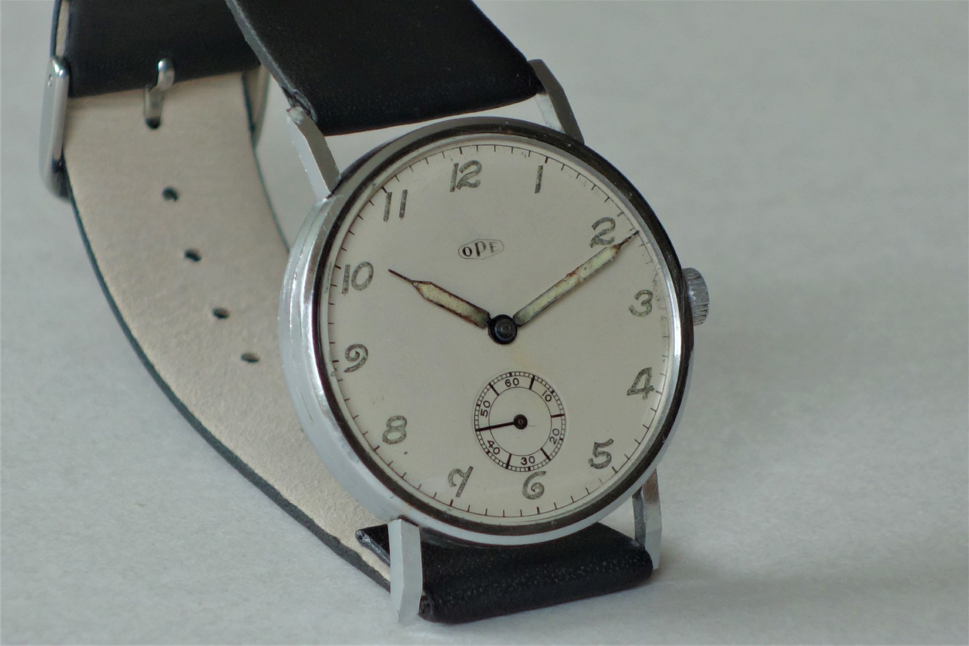 Silberfarbene mechanische Armbanduhr mit weißem Zifferblatt und schwarzem Armband.