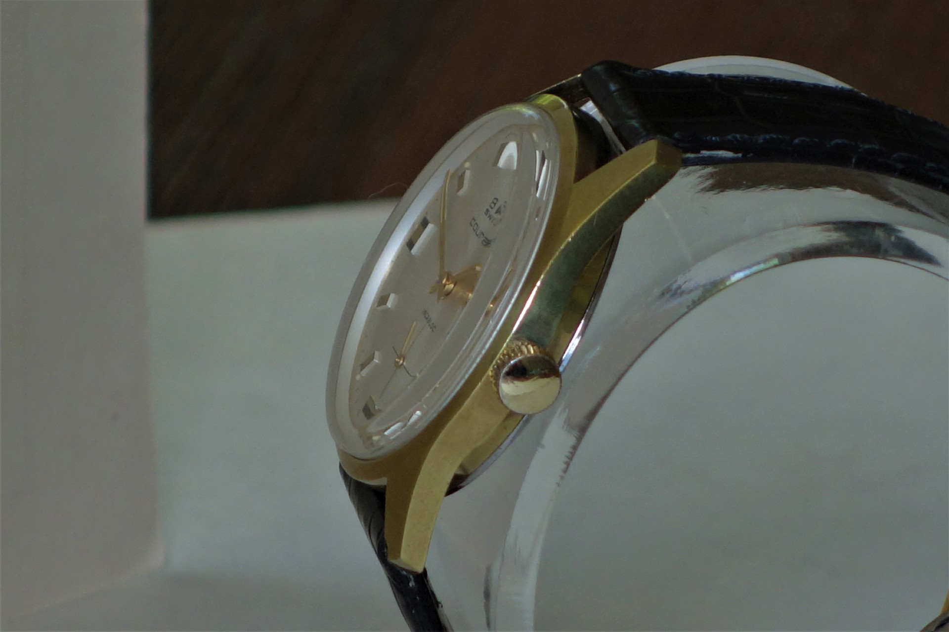 Analoge Armbanduhr mit goldfarbenem Gehäuse, hellem Zifferblatt und schwarzem Lederarmband.