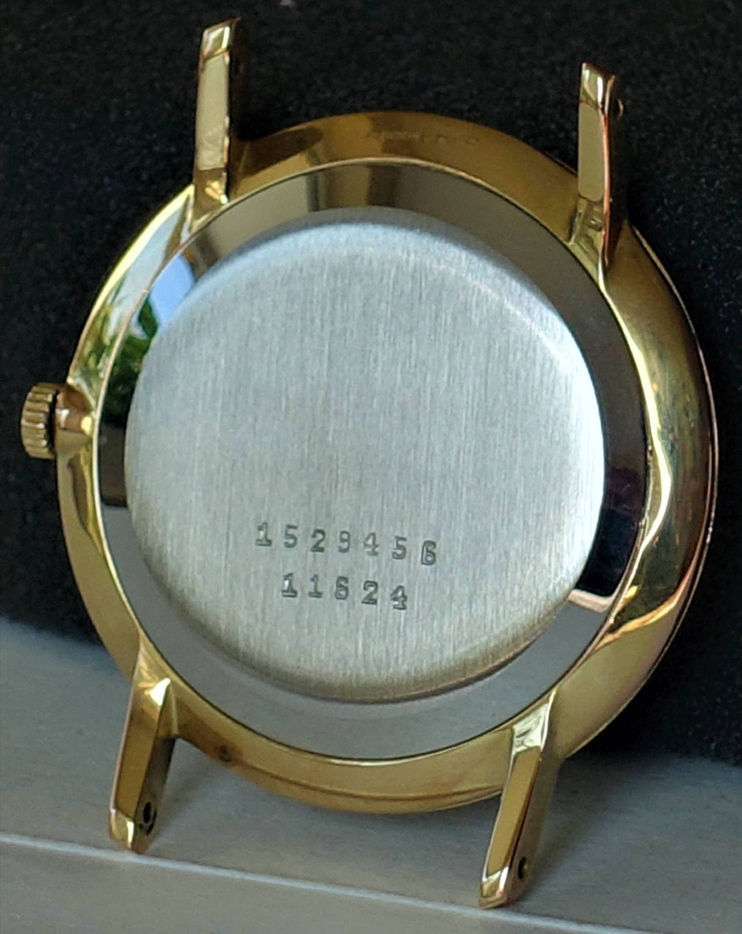 Rundes Uhrengehäuse in goldfarbener Optik mit silberfarbener Rückseite und seitlicher Krone.