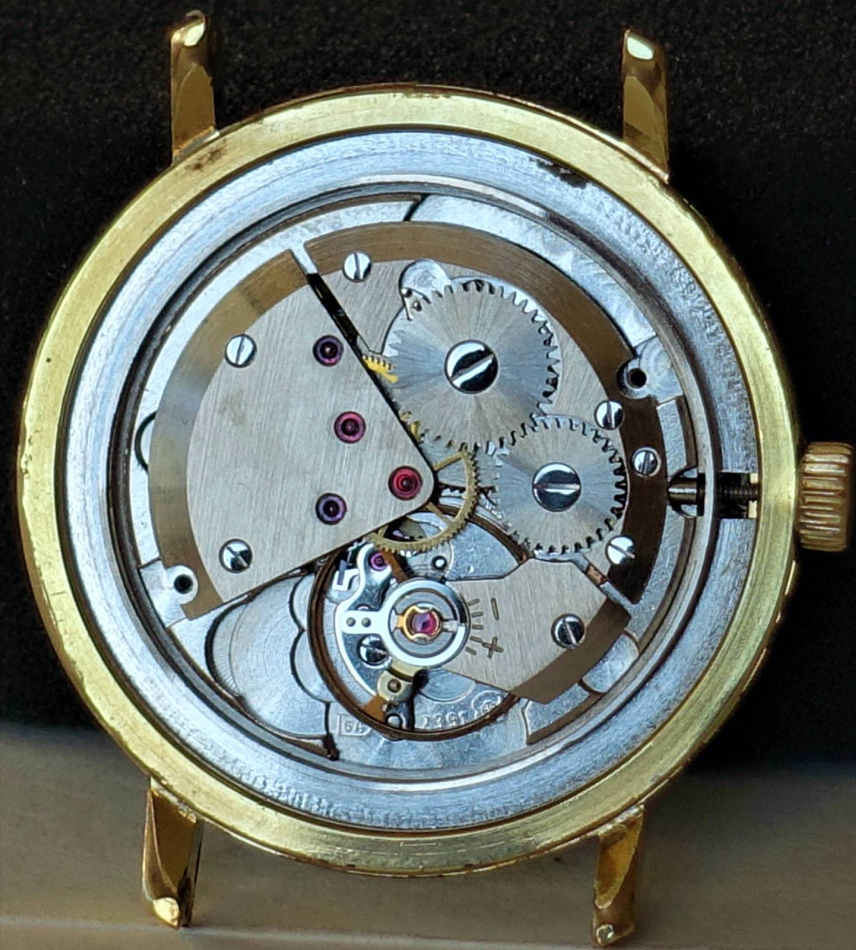 Mechanisches Uhrwerk in einem goldfarbenen Uhrengehäuse mit sichtbaren Zahnrädern und Schrauben.