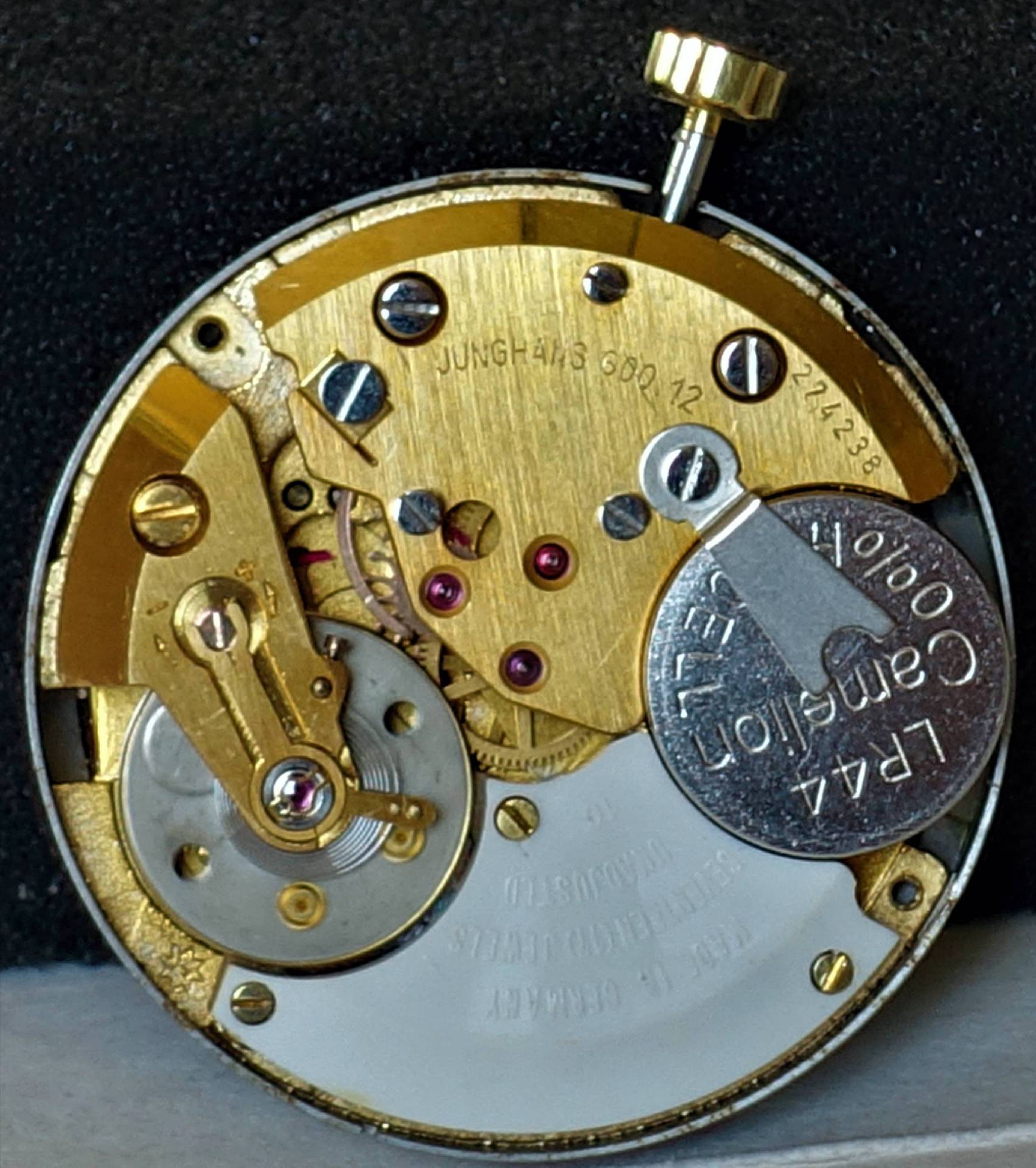 Goldfarbenes Uhrwerk mit sichtbarer Batterie und Aufzugswelle.