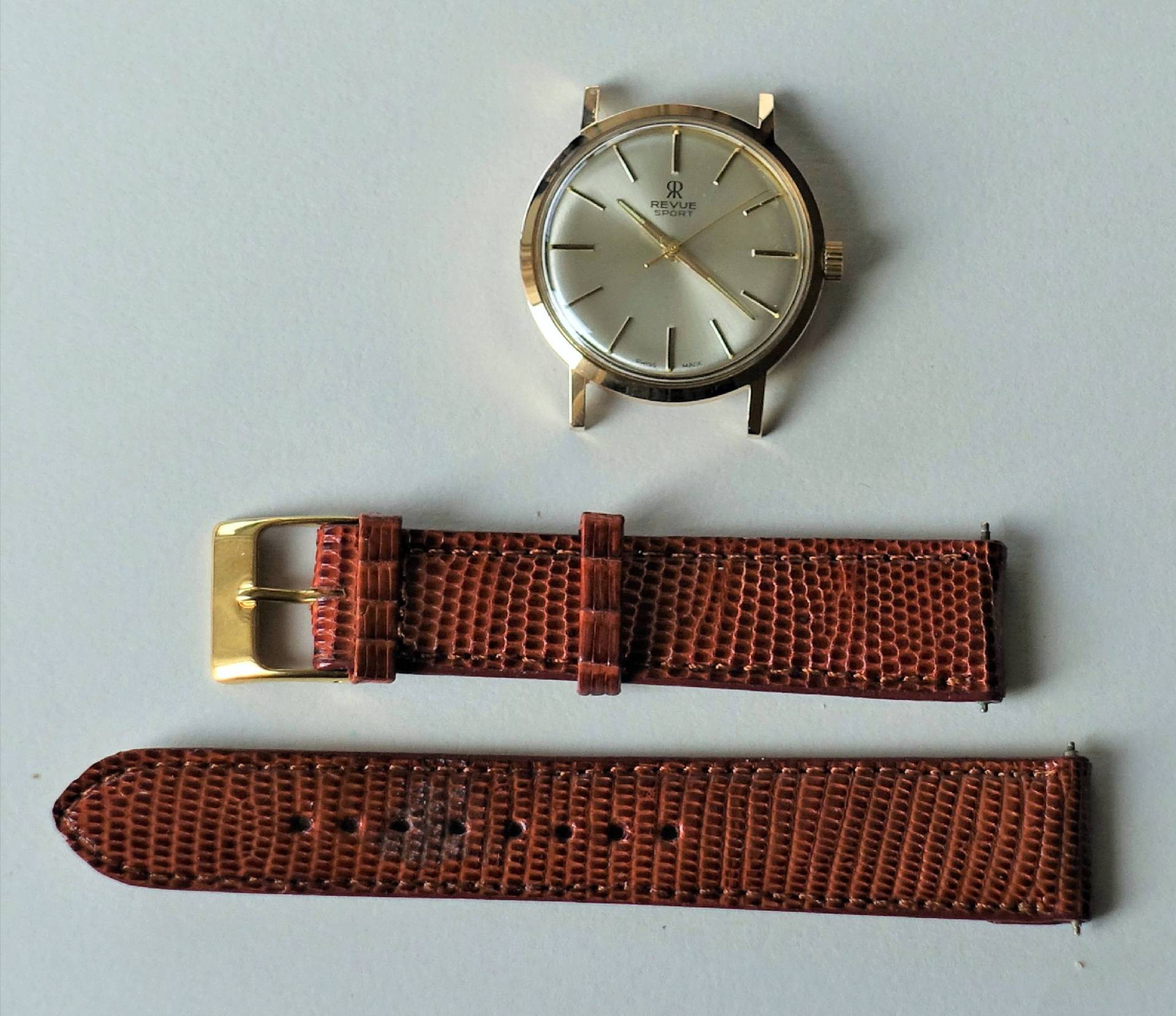 Goldfarbene Armbanduhr mit hellem Zifferblatt und braunem Lederarmband in zwei Teilen.