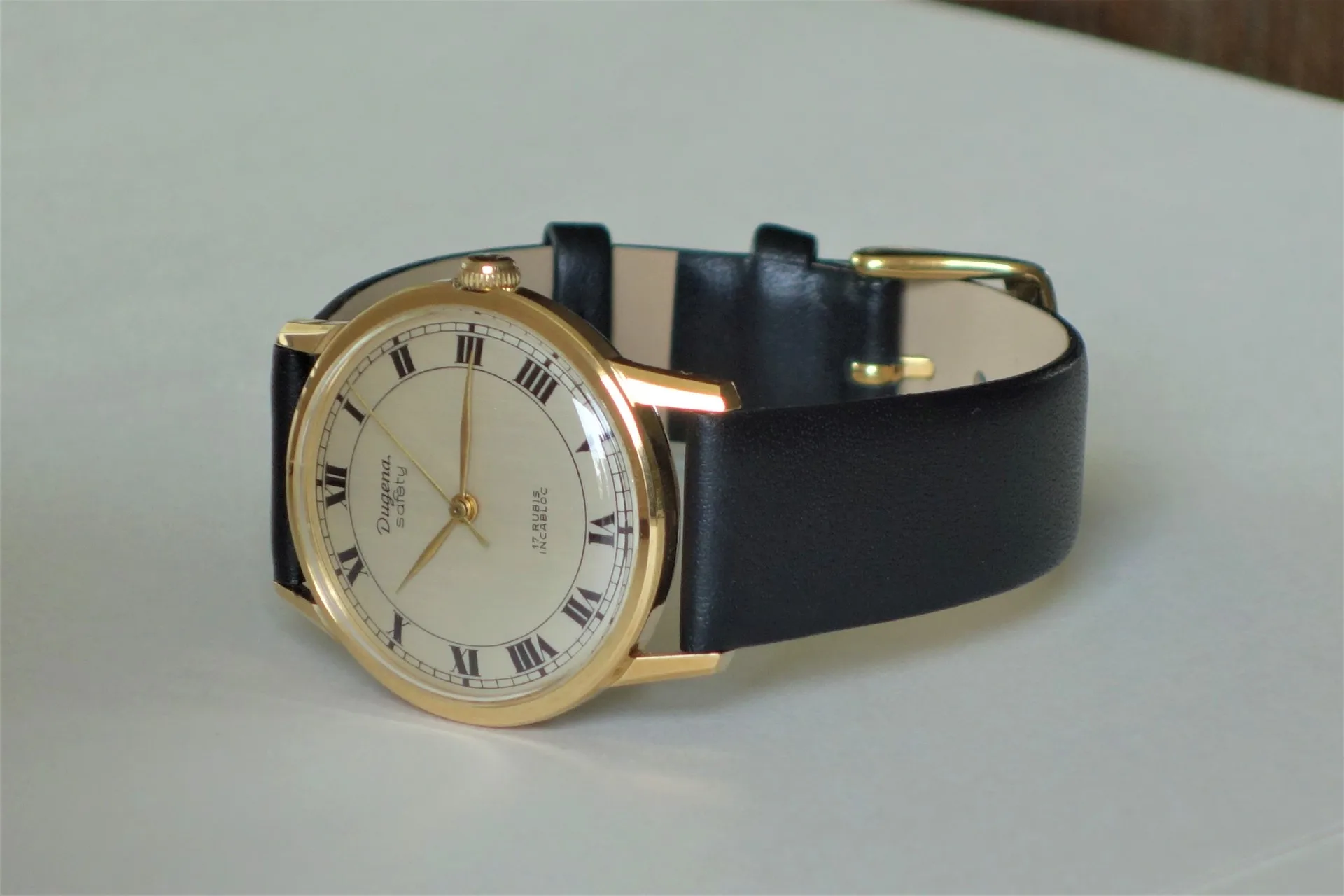 Klassische Armbanduhr mit goldfarbenem Gehäuse, hellem Zifferblatt und schwarzem Armband.
