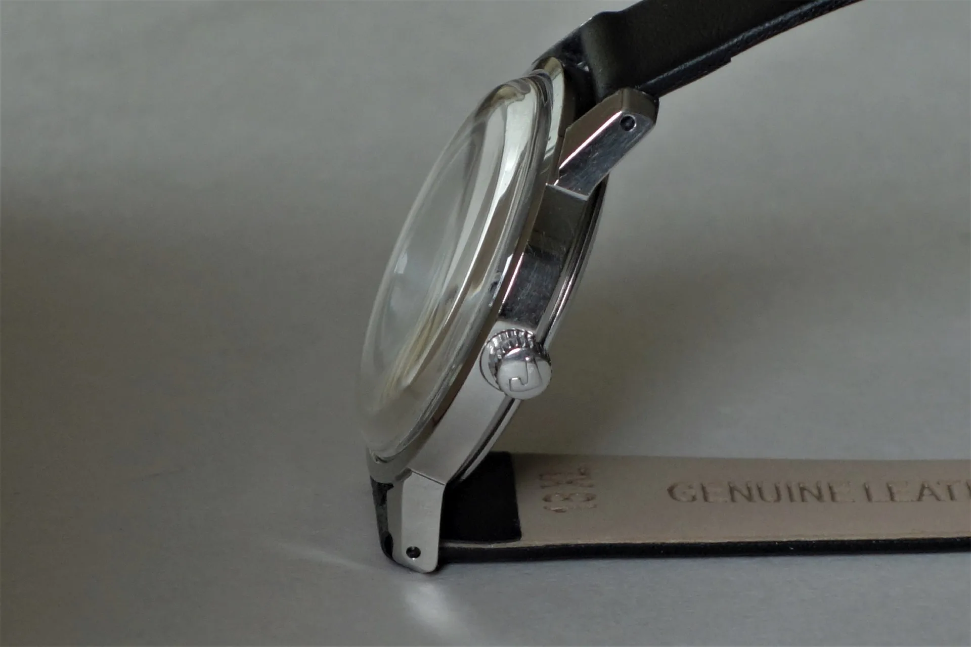 Seitliche Ansicht einer silberfarbenen Armbanduhr mit schwarzem Lederarmband und gewölbtem Uhrglas.