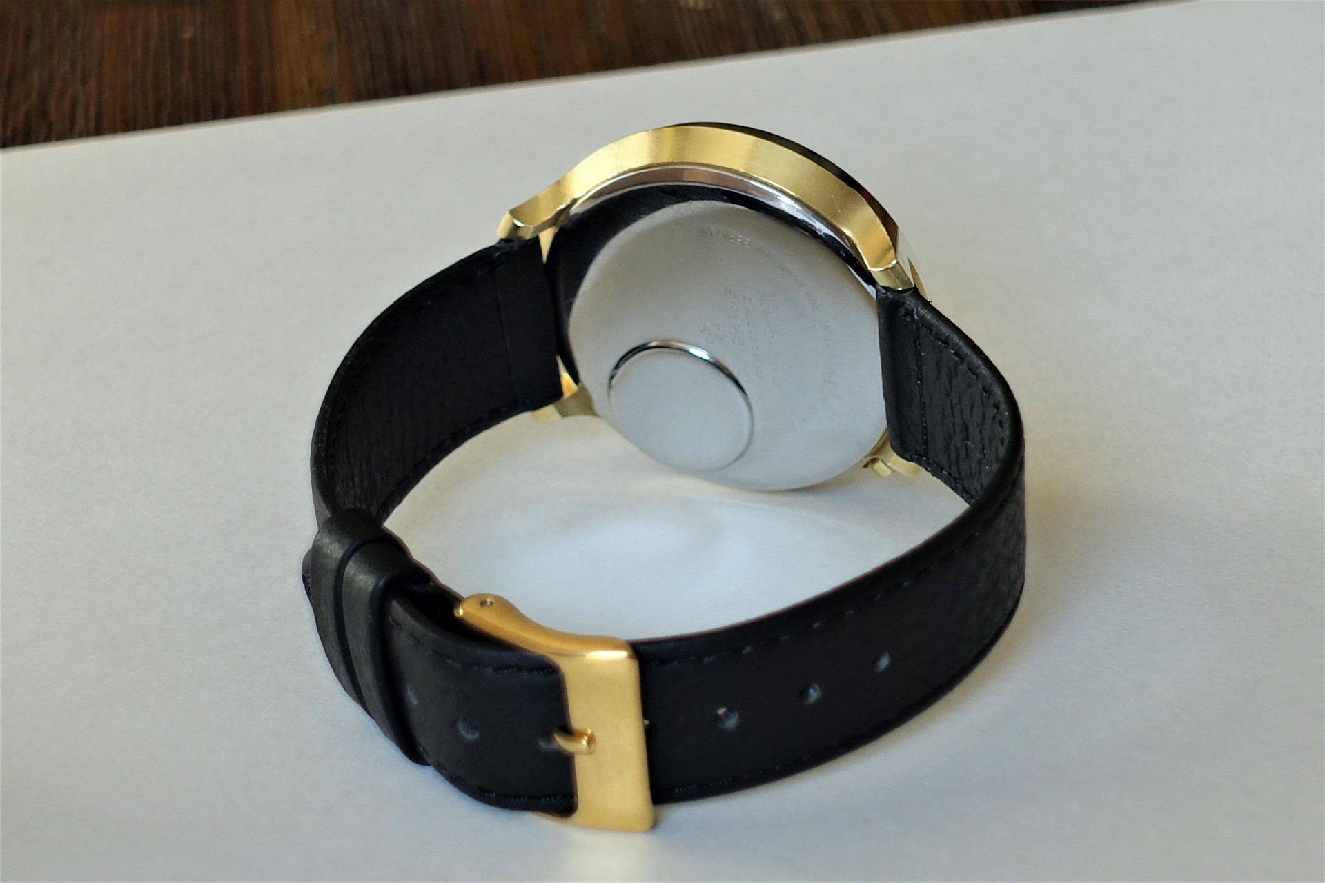 Armbanduhr mit schwarzem Armband, goldfarbenem Gehäuse und silberfarbener Rückseite.