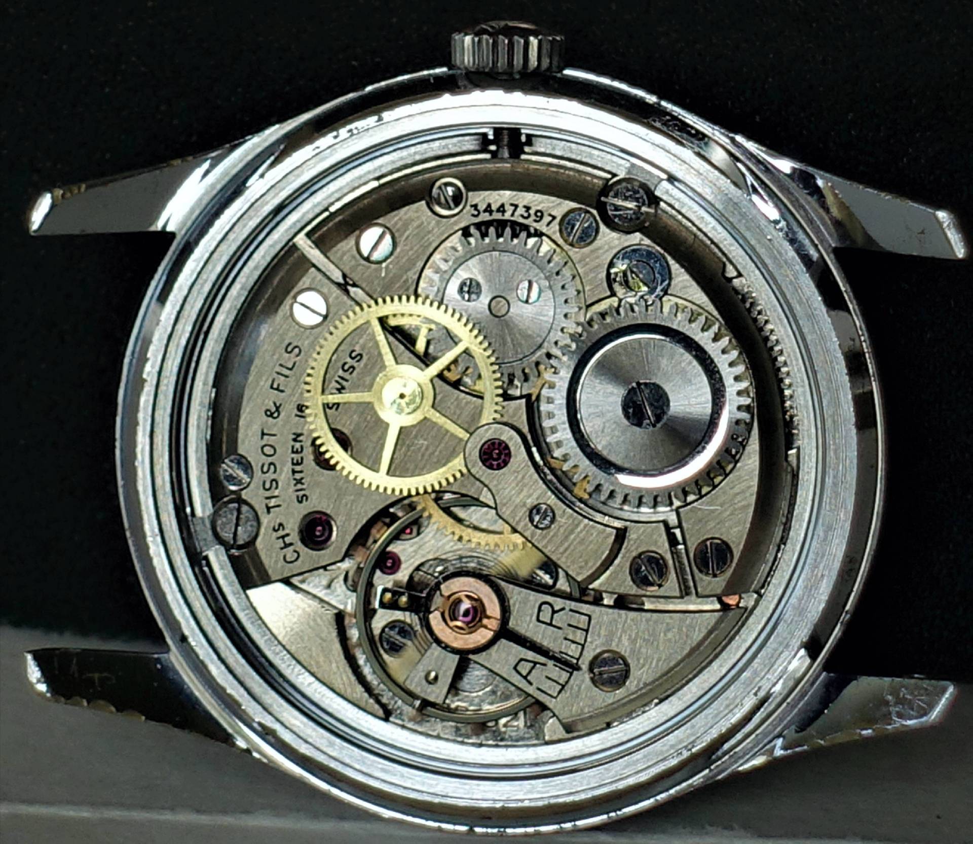 Offenes mechanisches Uhrwerk in silberfarbenem Gehäuse mit sichtbaren Zahnrädern und Gravuren.