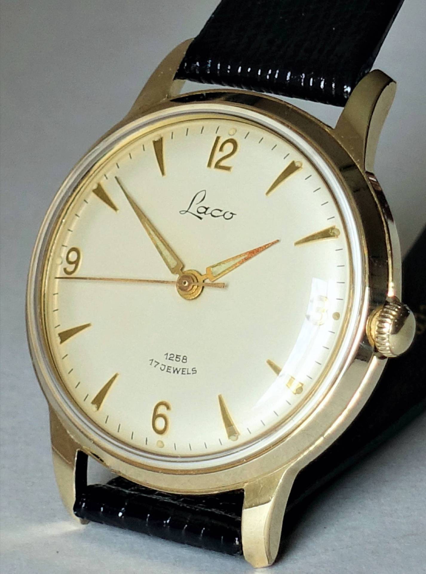 Goldfarbene Armbanduhr mit hellem Zifferblatt und schwarzem Armband.