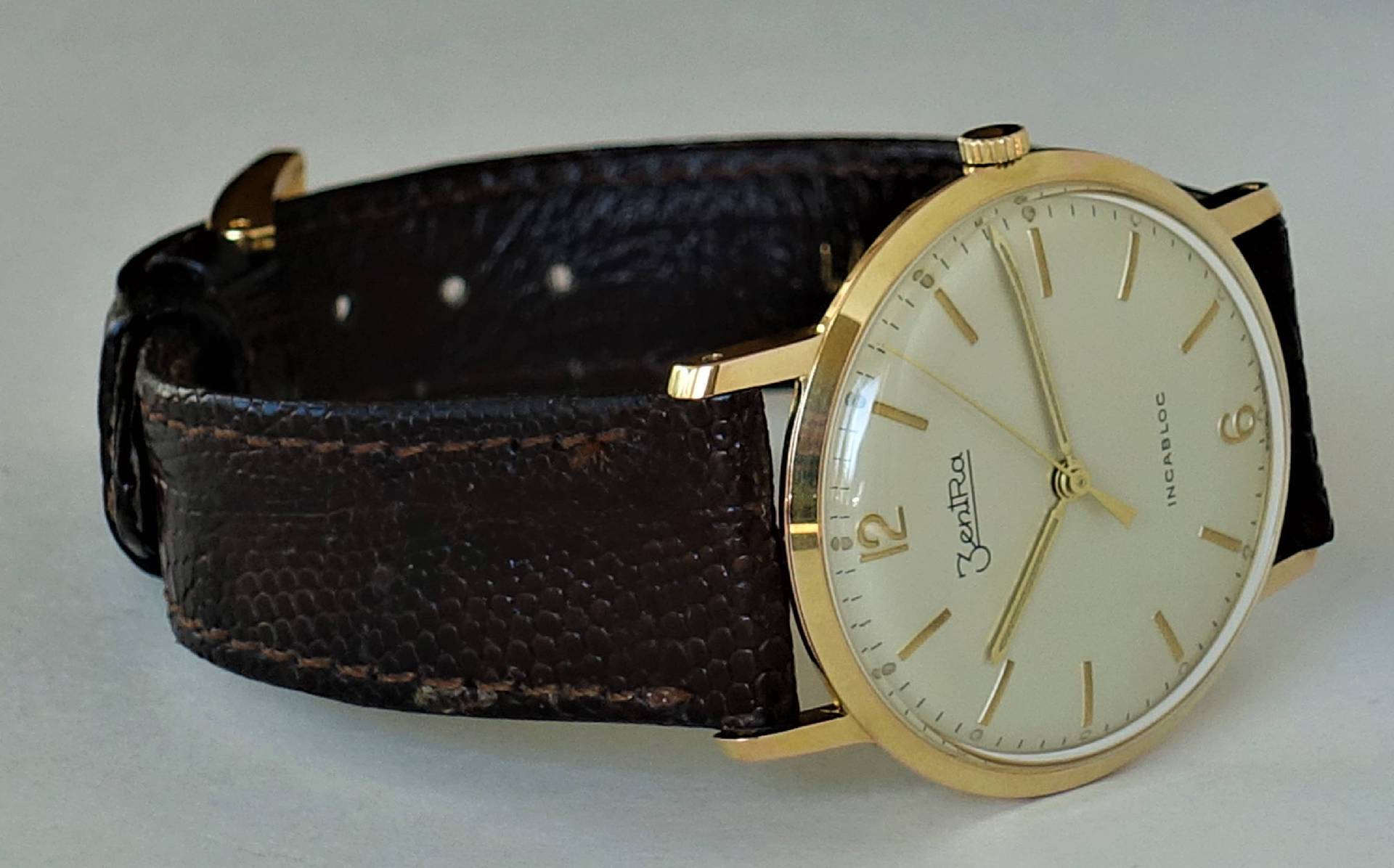 Goldfarbene Armbanduhr mit hellem Zifferblatt und braunem Armband.