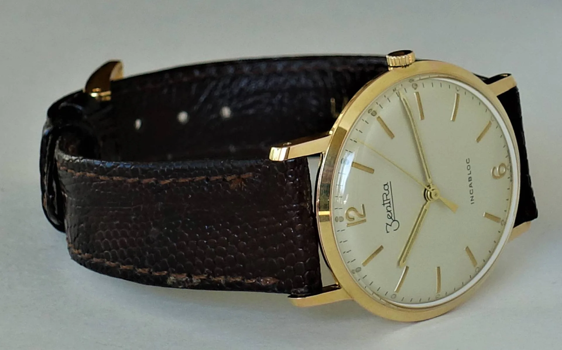 Goldfarbene Armbanduhr mit hellem Zifferblatt und braunem Armband.