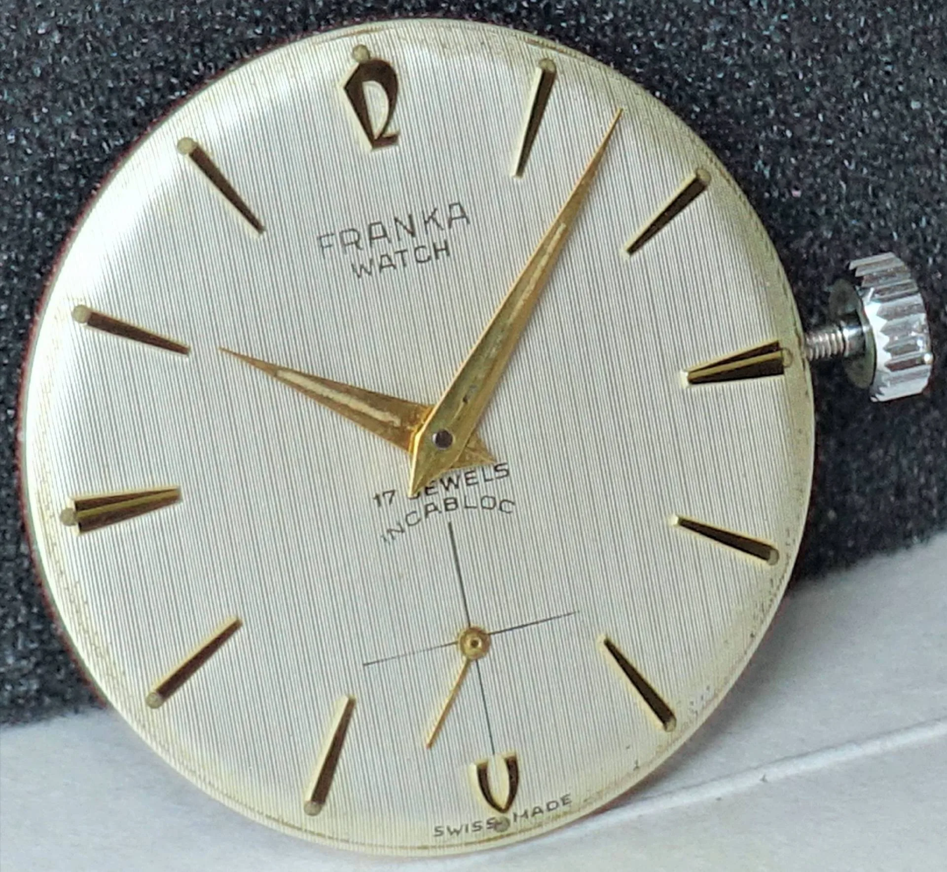 Franka Uhrwerk mit Zifferblatt Rundes Uhrwerk mit silberfarbenem Zifferblatt und goldfarbenen Zeigern, sichtbarer Krone und Aufschrift "Franka Watch".