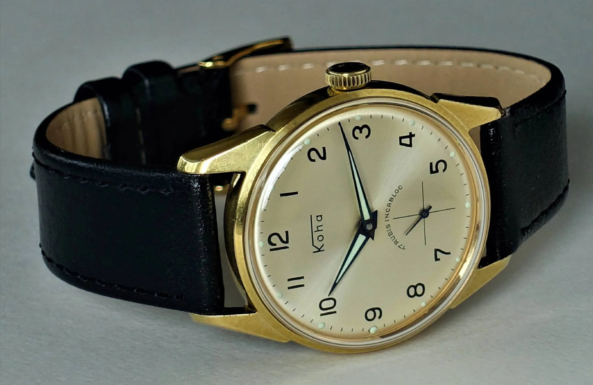 Goldfarbene Armbanduhr mit hellem Zifferblatt und schwarzem Armband.