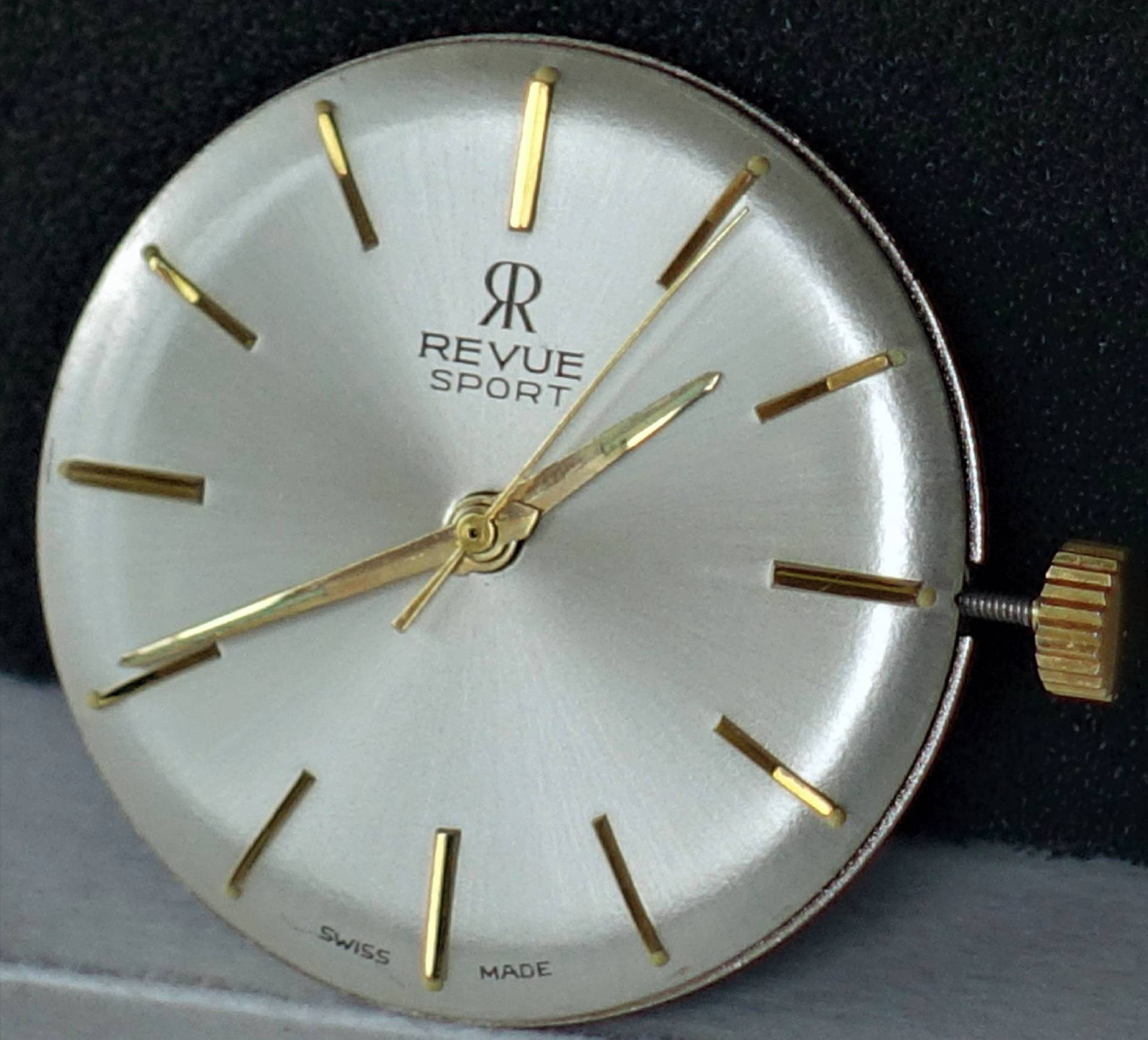 Rundes silberfarbenes Uhrwerk mit goldfarbenen Zeigern und Indizes, Aufschrift "Revue Sport".
