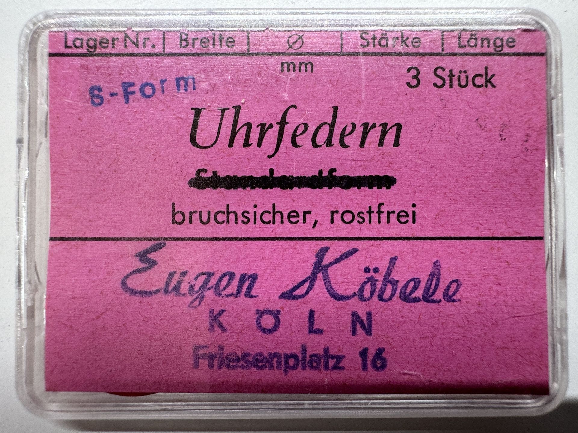 Drei bruchsichere, rostfreie Uhrfedern in S-Form in einer transparenten Kunststoffbox mit pinkem Etikett.