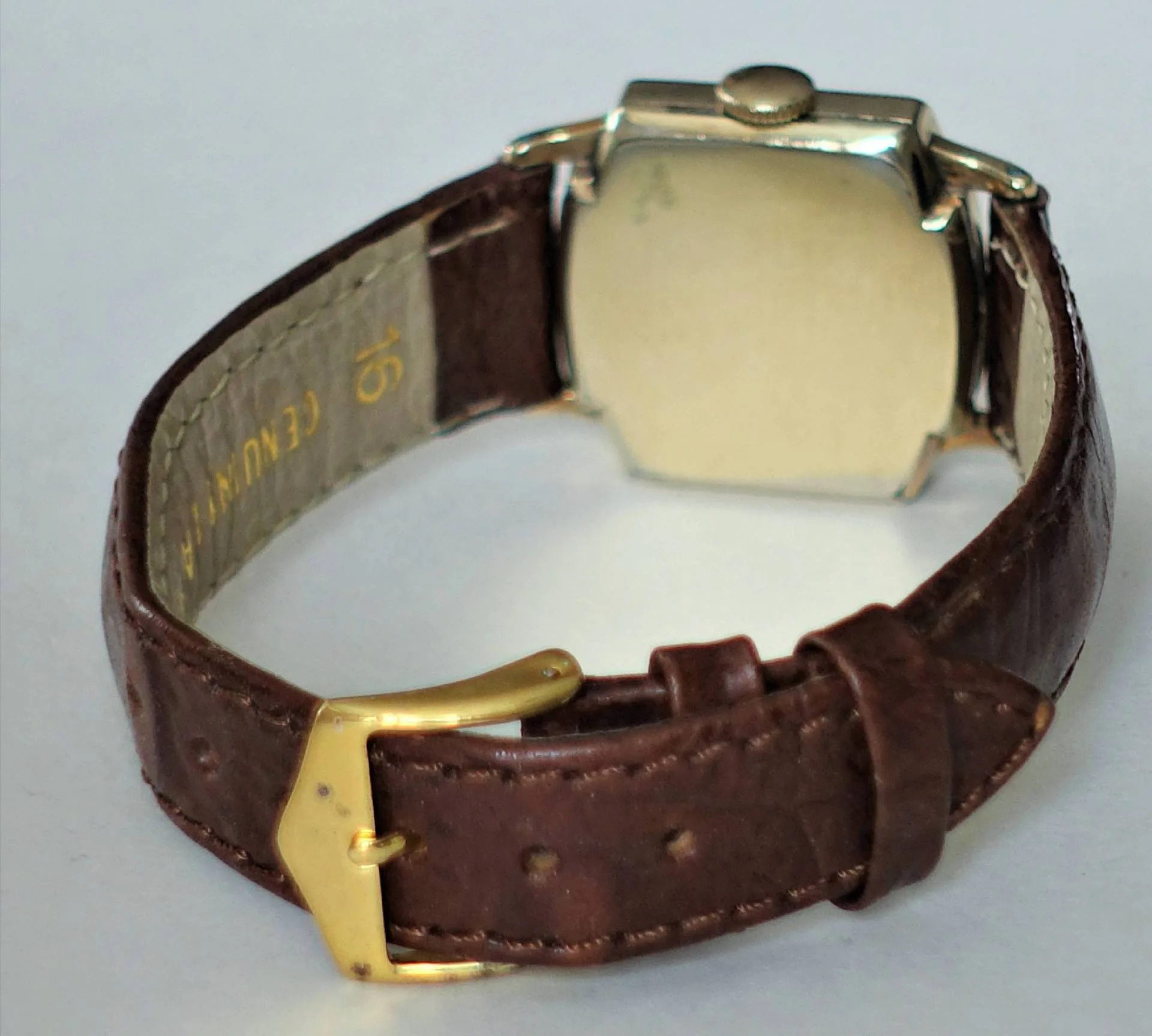 Eine Armbanduhr mit braunem Lederarmband, gelbfarbener Schließe und silberfarbenem Gehäuse, von hinten fotografiert.
