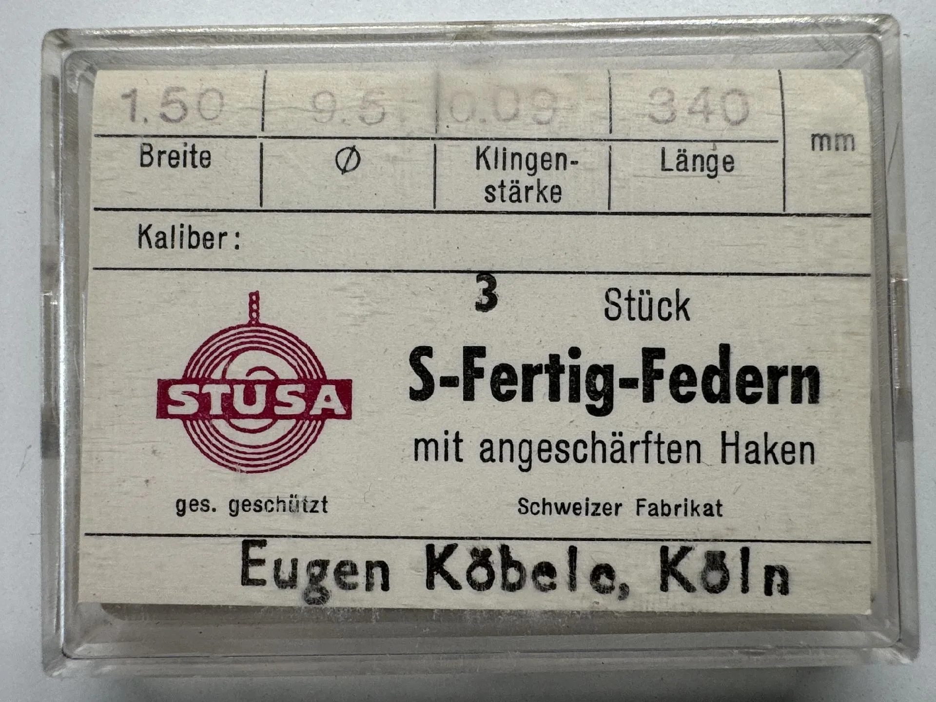 Verpackung mit drei Uhrmacher-Federn mit angeschärften Haken in transparenter Box.