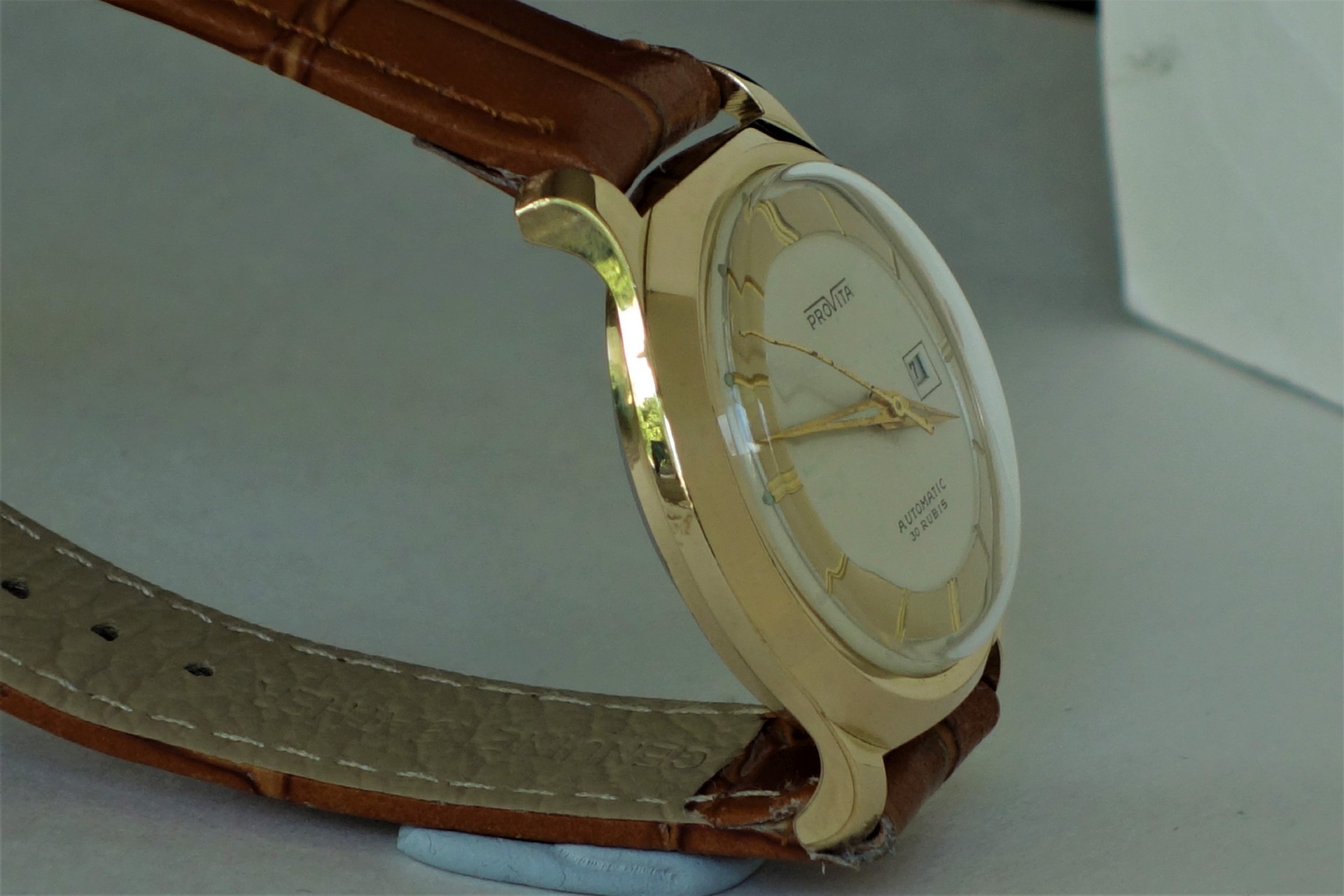 Goldfarbene Armbanduhr mit beigem Zifferblatt und braunem Armband.