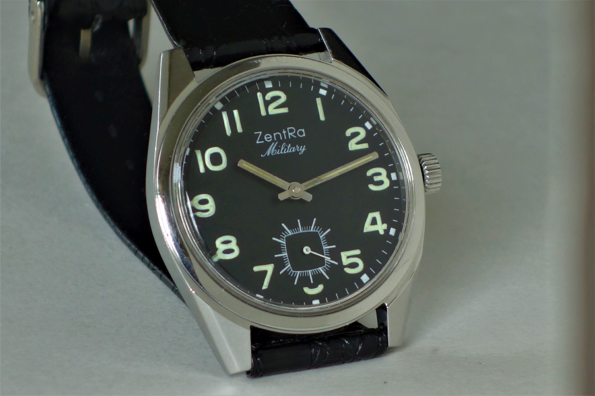 Schwarze Armbanduhr mit silberfarbenem Gehäuse und Leuchtziffern.