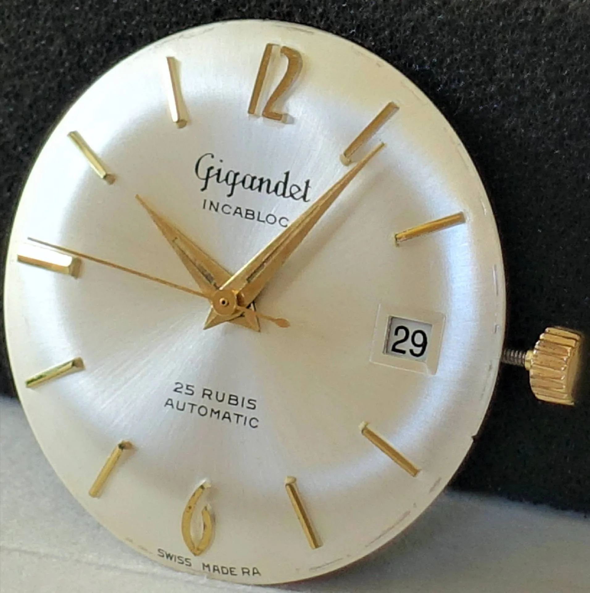 Rundes silberfarbenes Uhrwerk mit goldfarbenen Zeigern und Indizes, Datumsanzeige bei drei Uhr, Marke Gigandet.
