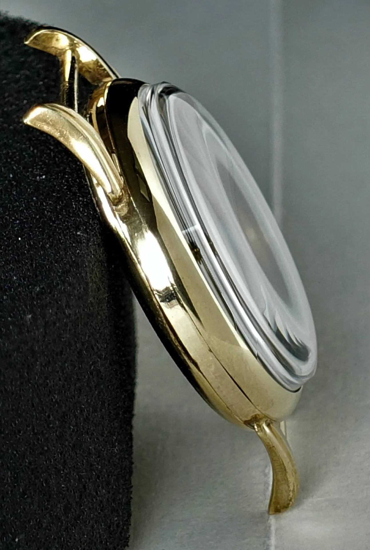 Seitliche Nahaufnahme eines glänzend gelbfarbenen Uhrengehäuses mit stark gewölbtem Glas und elegant gebogenen Bandanstößen.