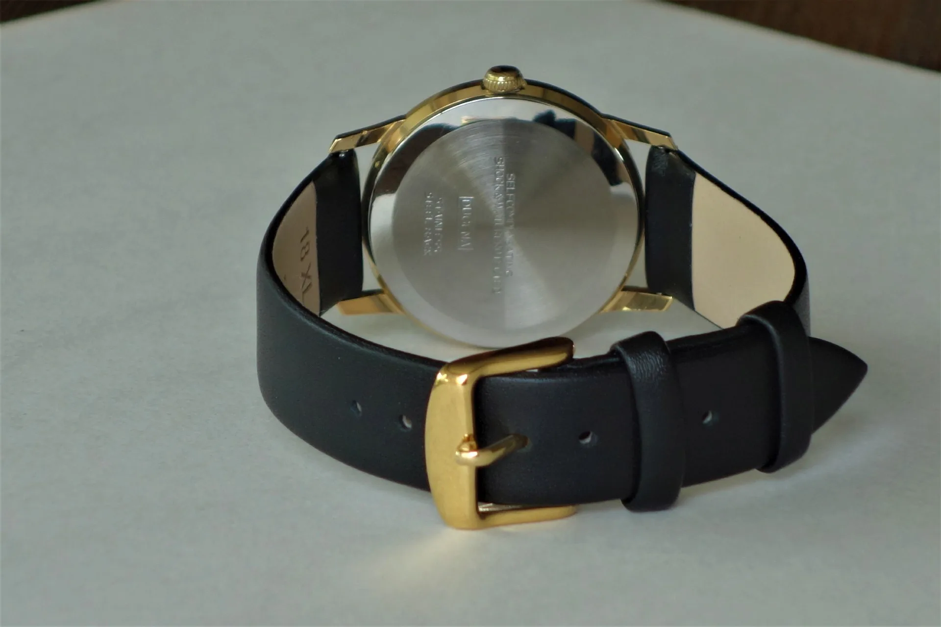 Armbanduhr schwarz gold Schwarze Armbanduhr mit goldfarbenem Gehäuse und Schnalle, Rückseite aus silberfarbenem Metall.