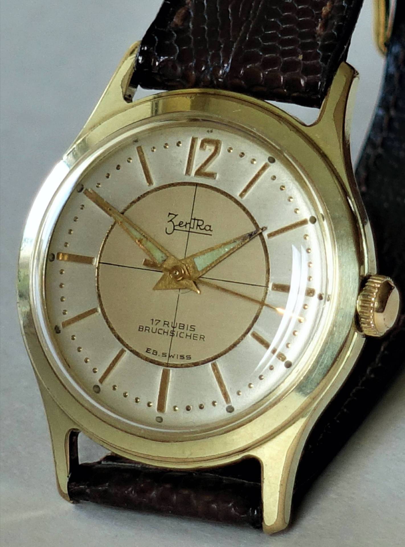 Goldfarbene Armbanduhr mit hellem Zifferblatt und braunem Armband.