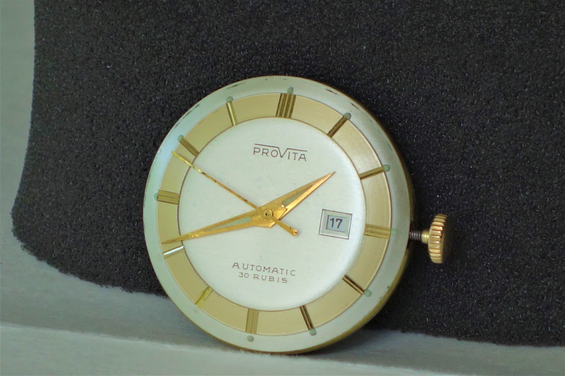 Rundes Uhrwerk mit weiß-goldenem Zifferblatt, goldfarbenen Zeigern und Datumsanzeige.