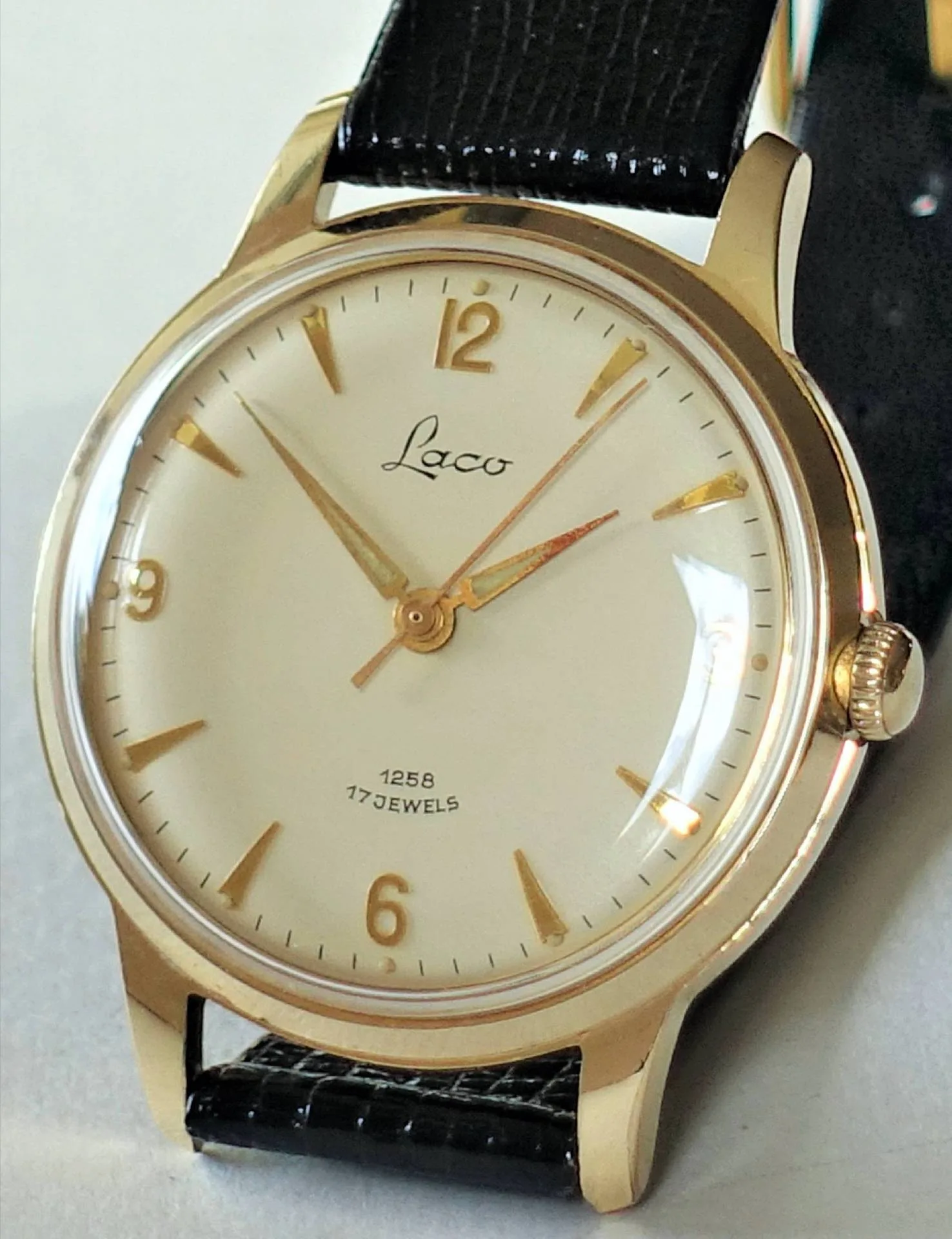 Laco Armbanduhr goldfarben Goldfarbene Armbanduhr mit hellem Zifferblatt, goldenen Indizes und schwarzem Armband.