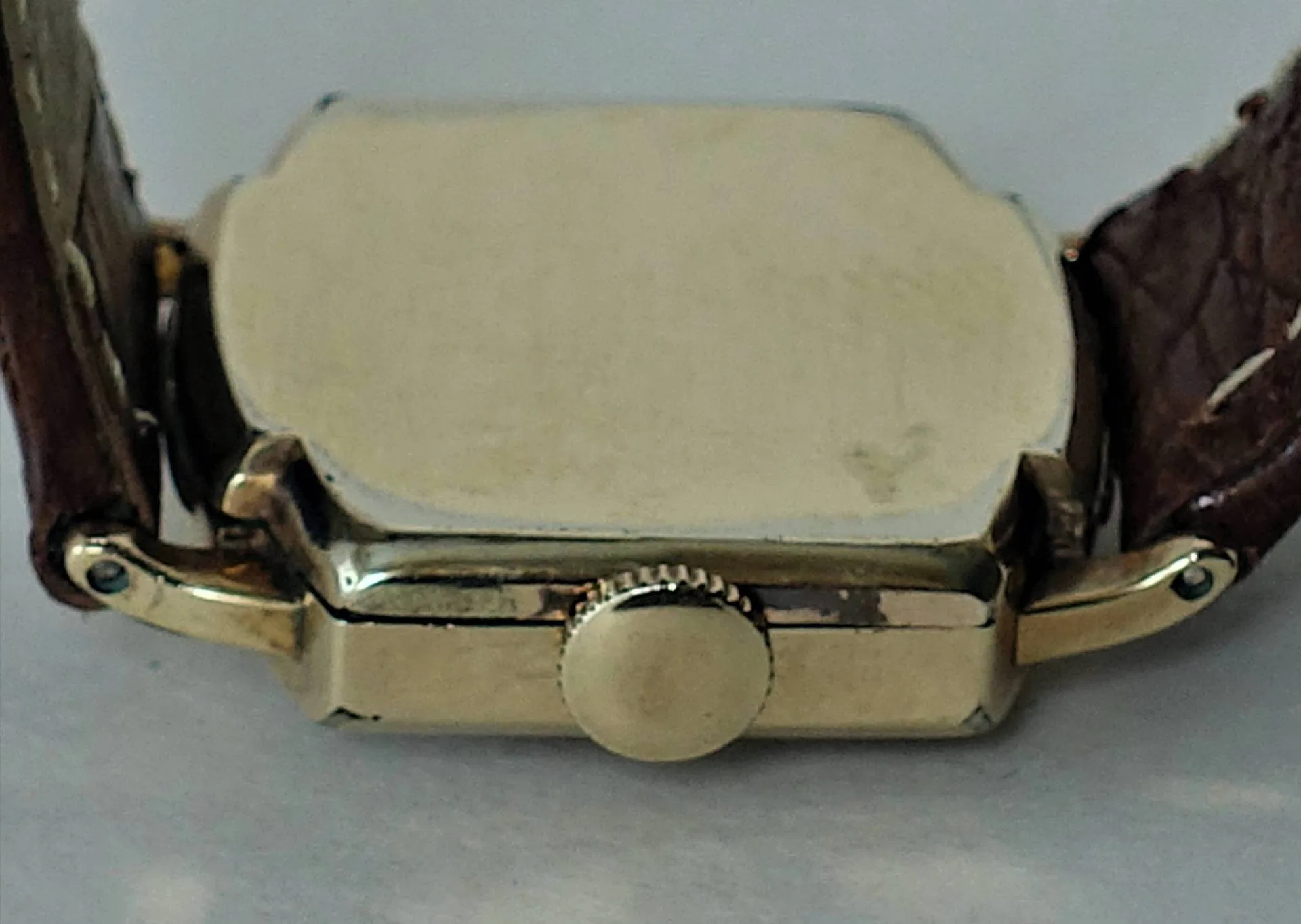 Die Nahaufnahme zeigt die Rückseite einer rechteckigen Armbanduhr mit gelbgoldfarbenem Gehäuse und braunem Lederarmband.