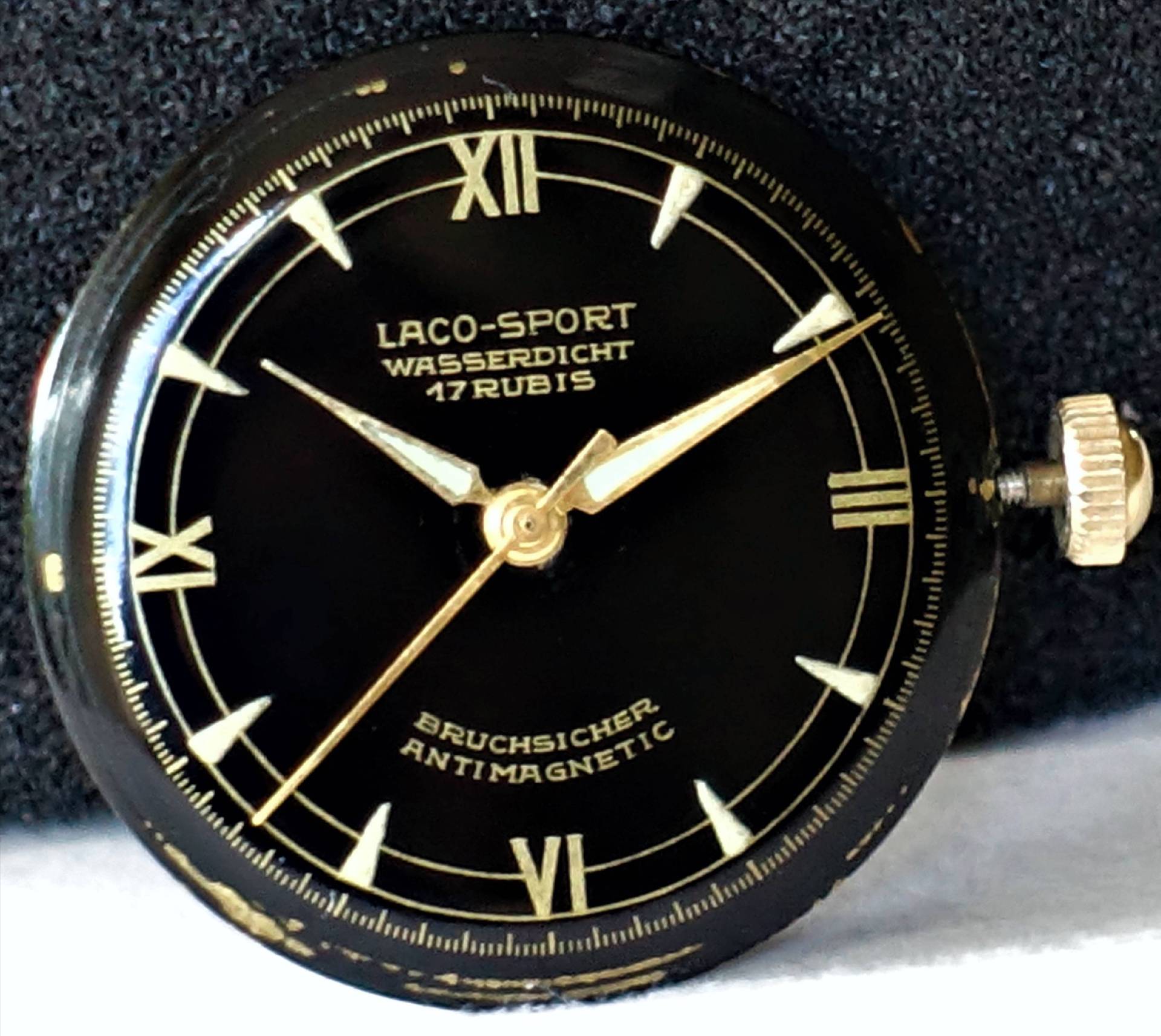Schwarzes Zifferblatt einer Laco-Sport Armbanduhr mit goldfarbenen Zeigern und römischen Ziffern.