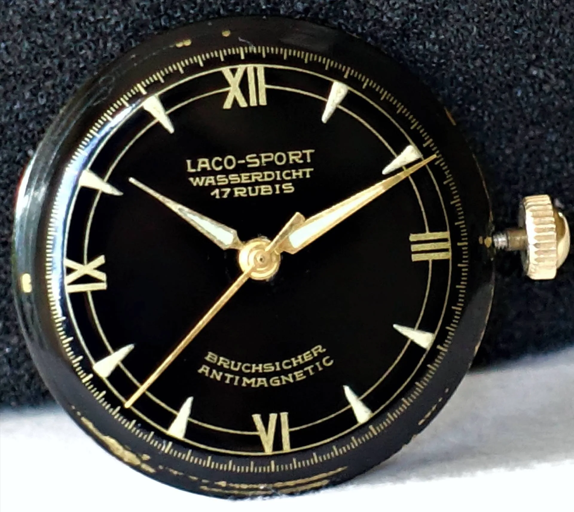 Schwarzes Zifferblatt einer Laco-Sport Armbanduhr mit goldfarbenen Zeigern und römischen Ziffern.