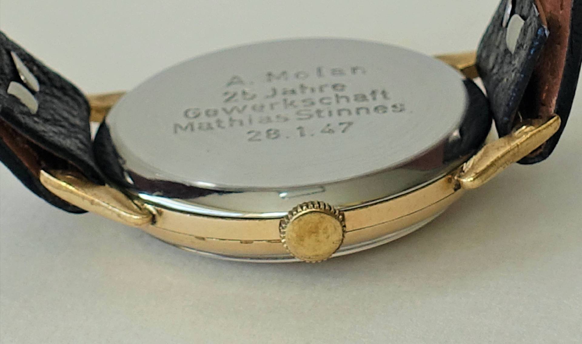 Rückseite einer Armbanduhr mit silberfarbenem Boden, goldfarbener Krone und schwarzem Armband.