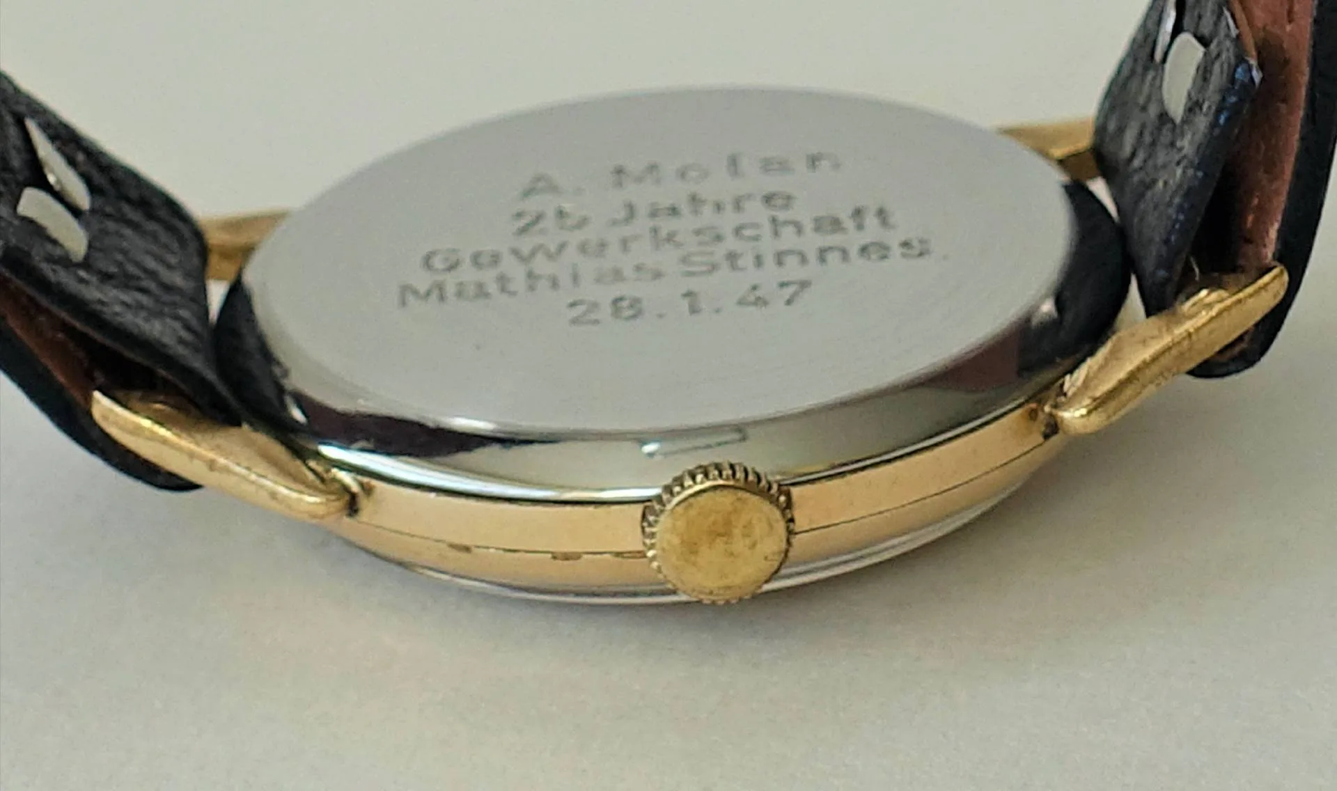 Armbanduhr Rückseite zweifarbig Rückseite einer Armbanduhr mit silberfarbenem Boden, goldfarbener Krone und schwarzem Armband.