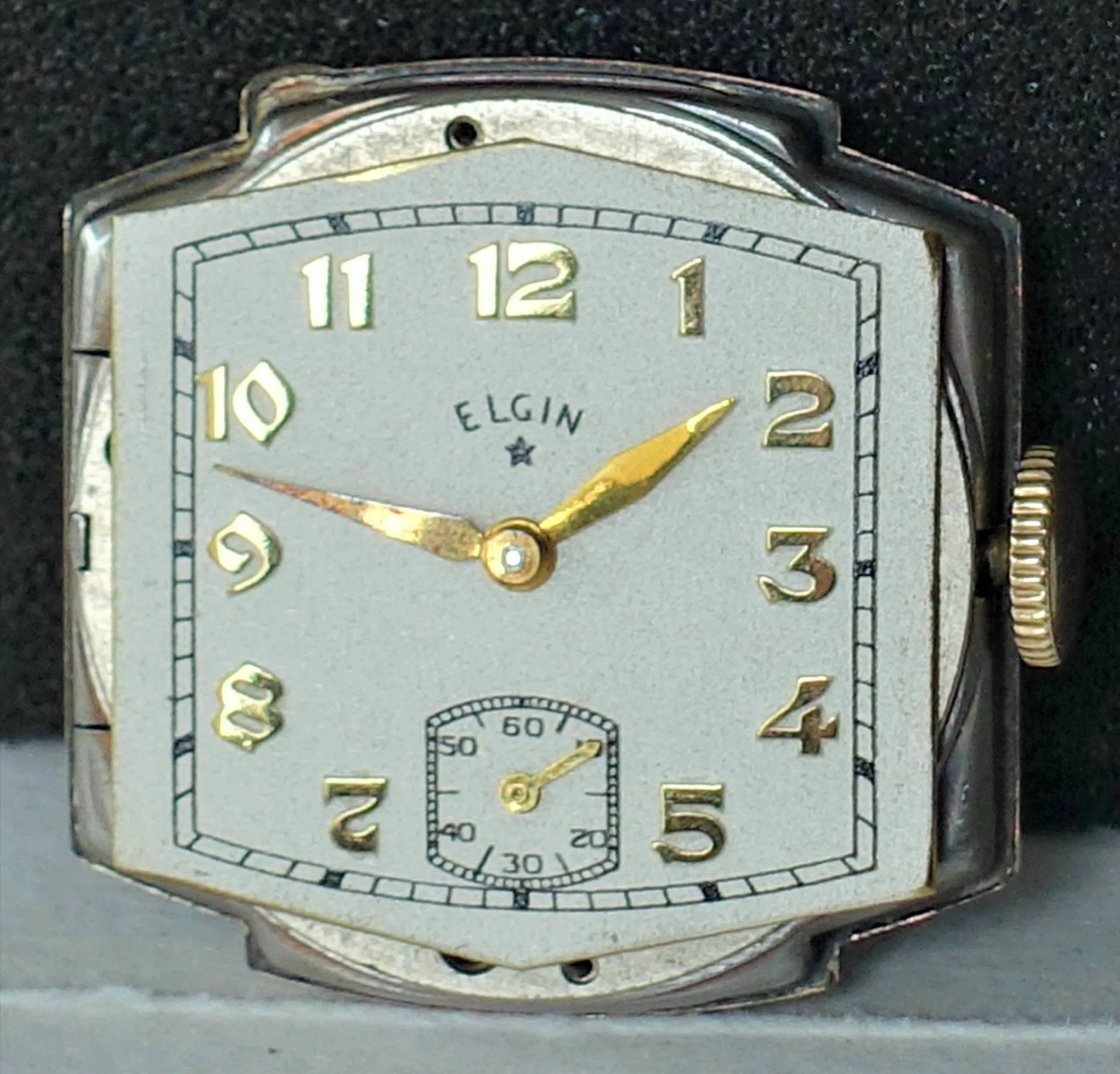 Rechteckiges Uhrwerk mit silberfarbenem Gehäuse, goldenen Zeigern und Ziffern sowie kleiner Sekunde bei sechs Uhr.