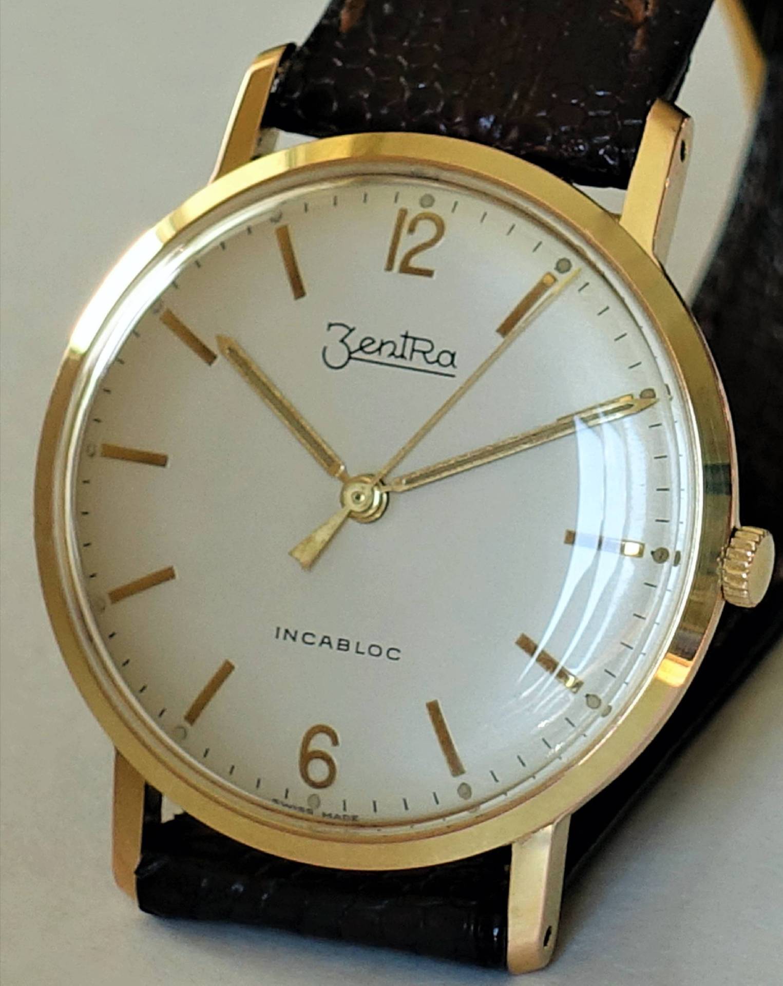 Goldfarbene Armbanduhr mit weißem Zifferblatt und schwarzem Armband.