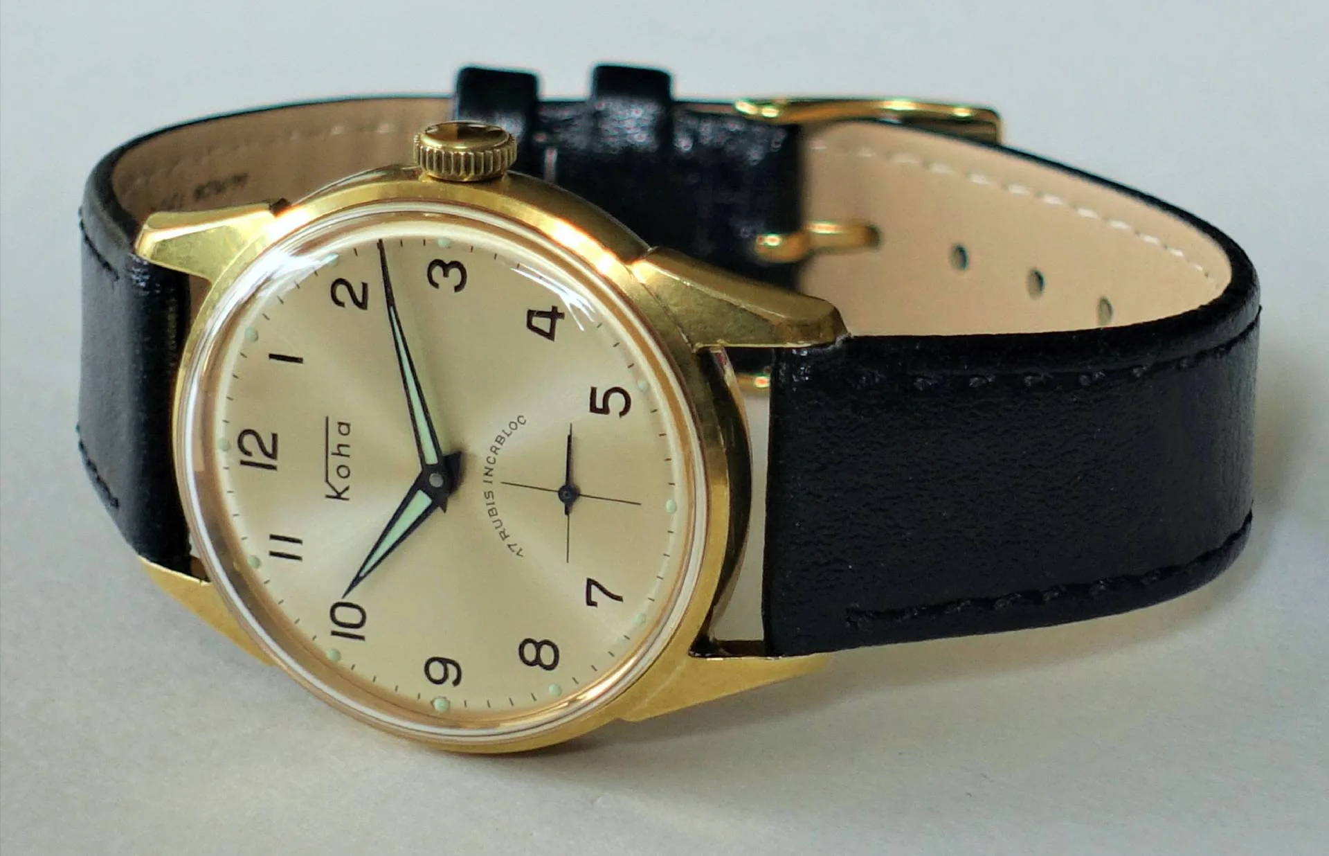 Analoge Armbanduhr mit goldfarbenem Gehäuse, hellem Zifferblatt und schwarzem Armband.