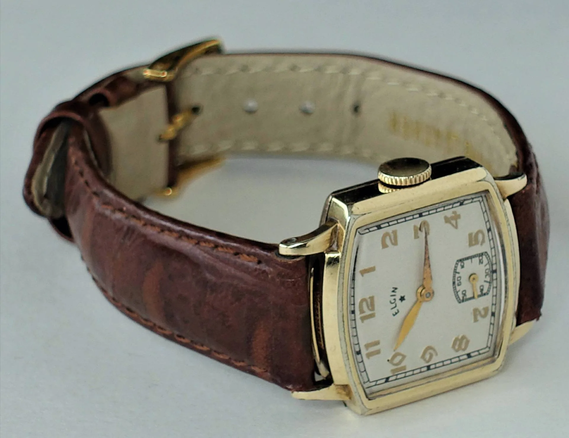 Rechteckige gelbe Uhr, braunes Leder Eine rechteckige Armbanduhr mit gelbem Gehäuse, weißem Zifferblatt und braunem Lederarmband liegt auf einer hellen Oberfläche.