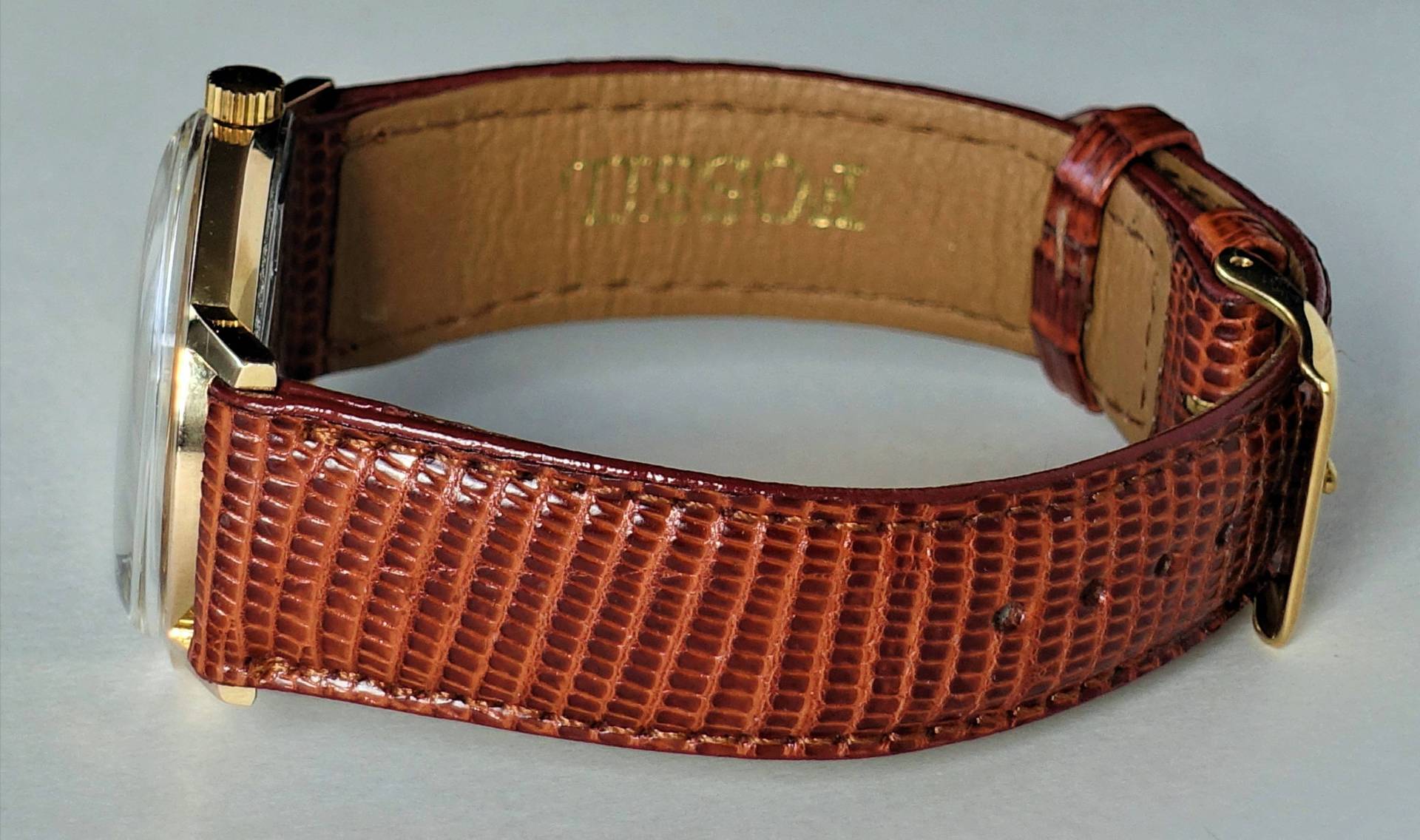 Braune Armbanduhr mit goldfarbenem Gehäuse und strukturierter Oberfläche.