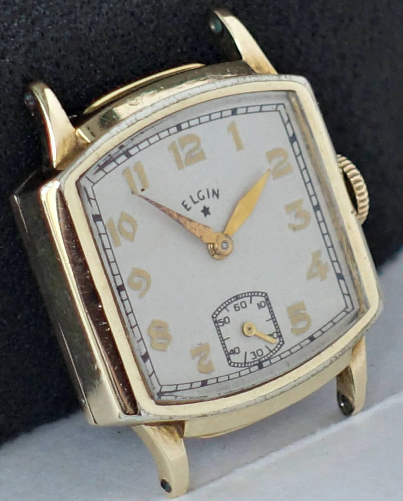 Eine eckige Armbanduhr mit gelbem Gehäuse, beigem Zifferblatt und goldfarbenen Zeigern, darunter eine kleine Sekunde.