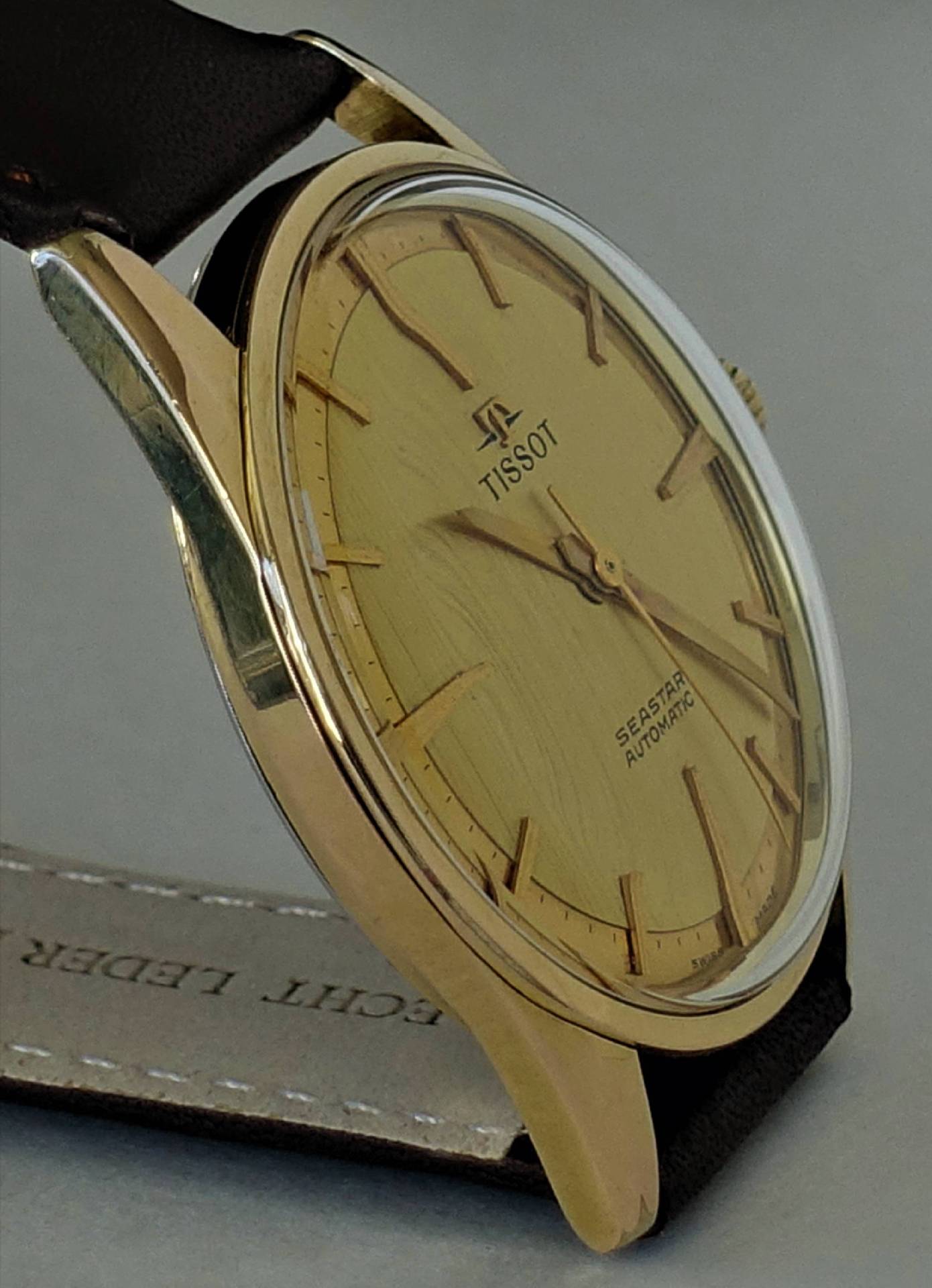 Goldfarbene Armbanduhr mit hellem Zifferblatt und schwarzem Armband.