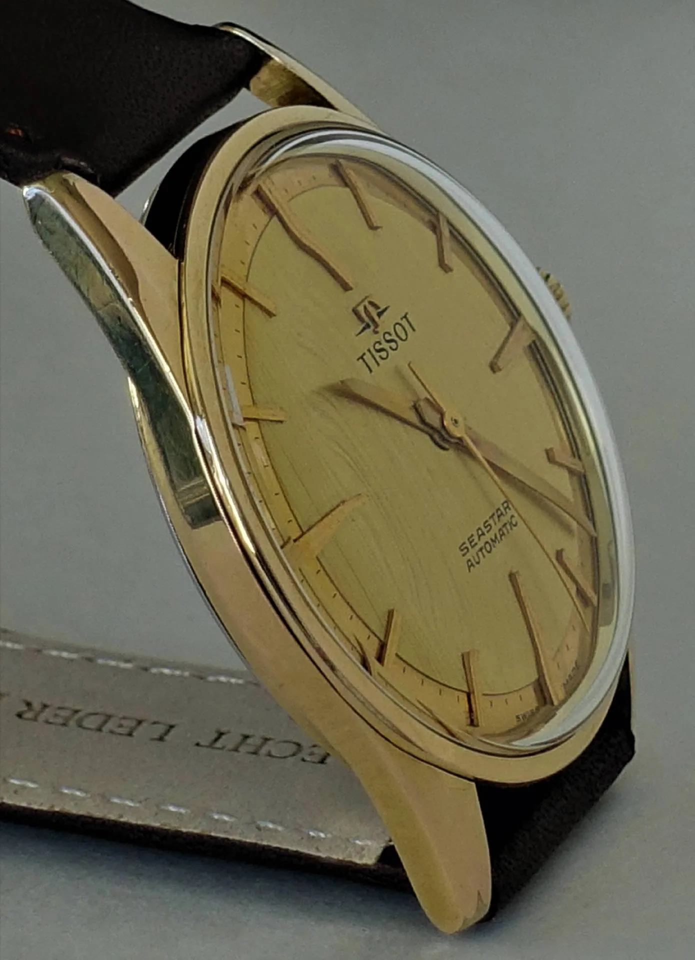 Goldfarbene Armbanduhr mit hellem Zifferblatt und schwarzem Armband.