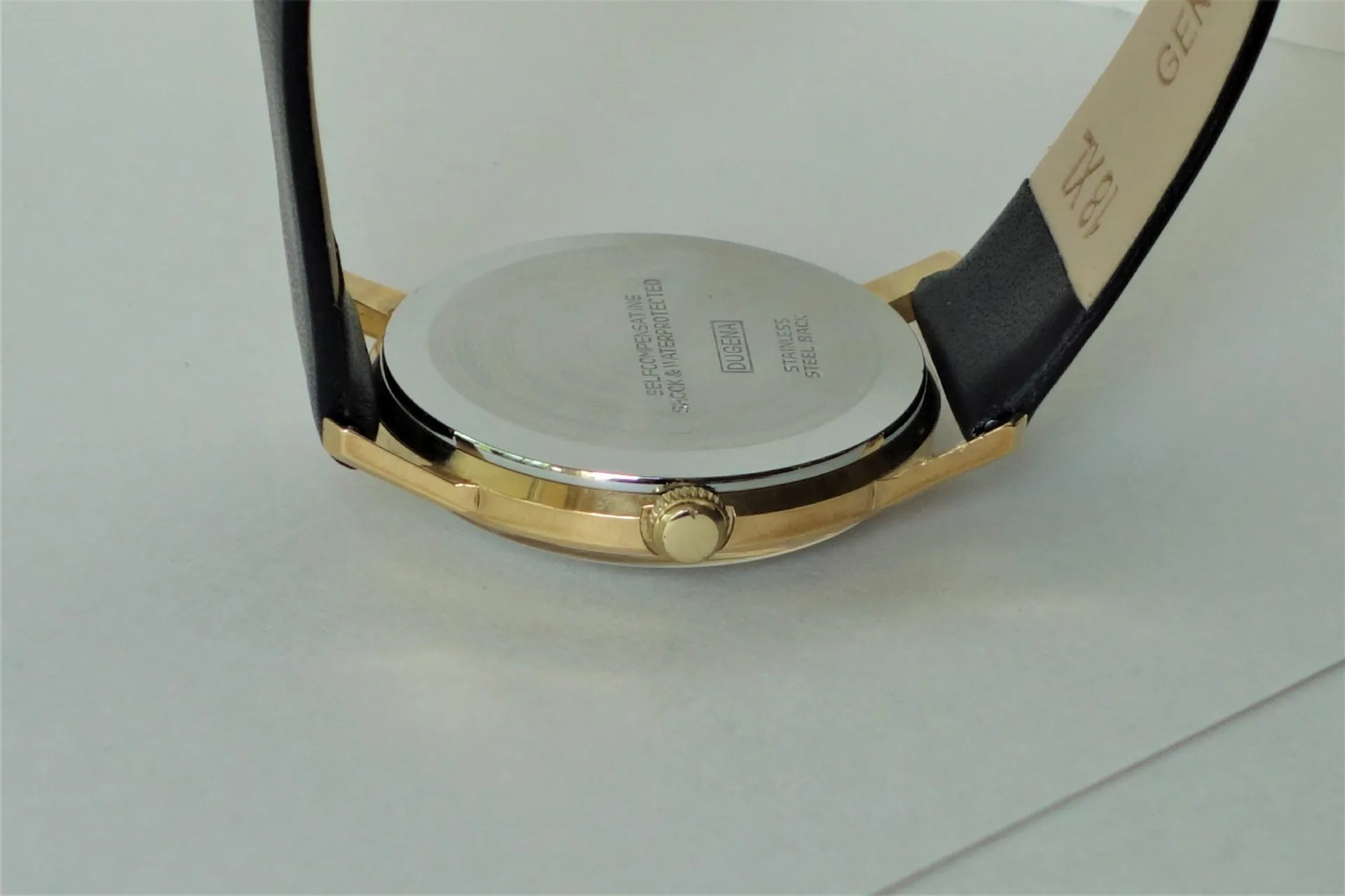 Rückseite eines goldfarbenen Uhrgehäuses mit silberfarbenem Boden und schwarzem Armband.