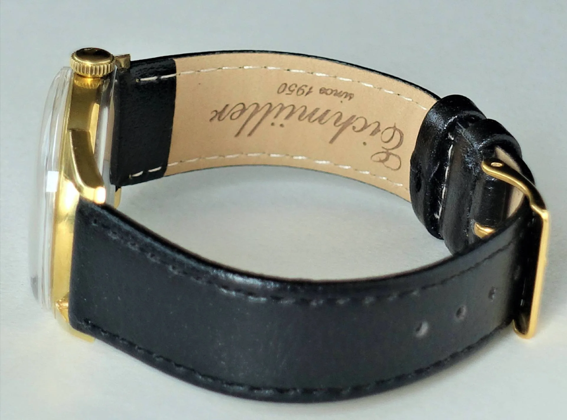 Schwarze Armbanduhr mit goldfarbenem Gehäuse und schwarzem Lederarmband.