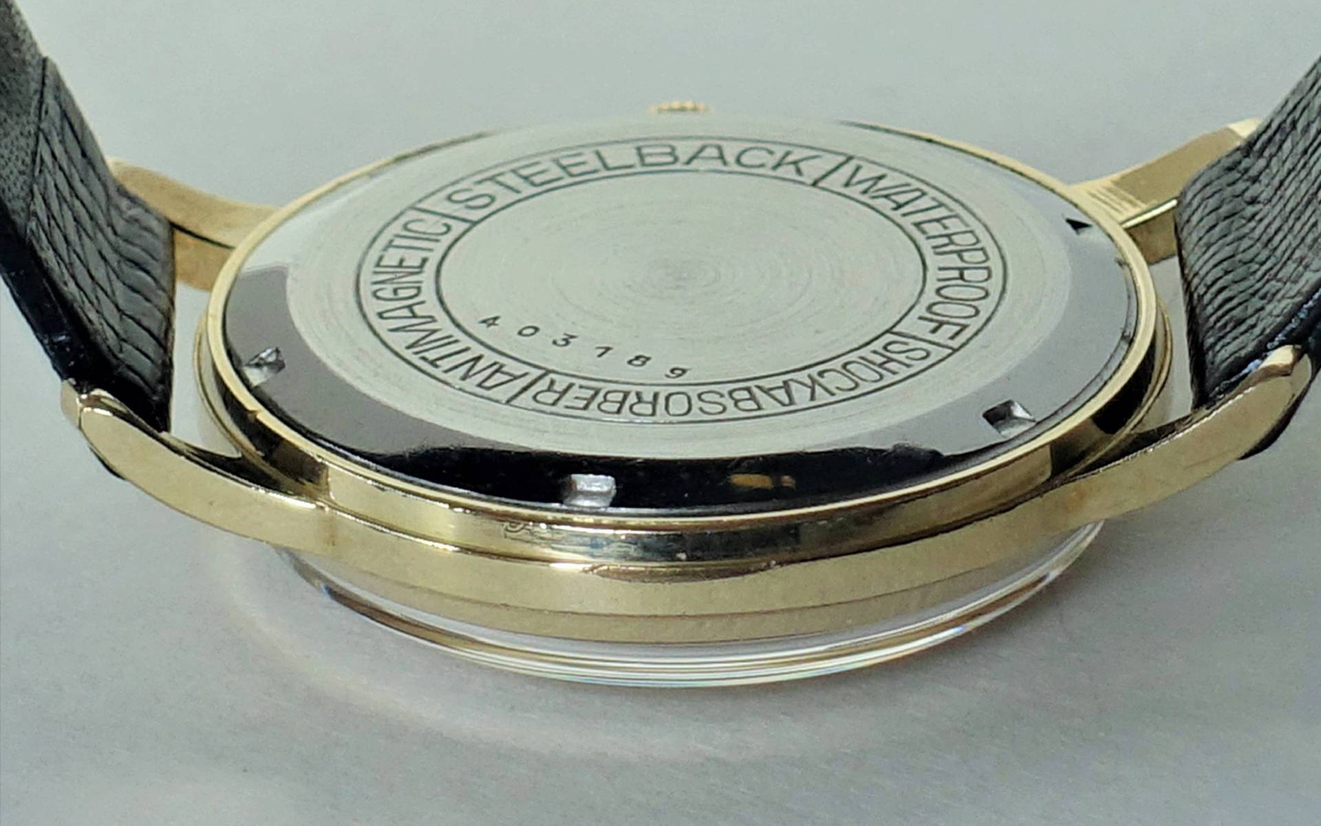 Silberfarbener Uhrboden mit Gravur und schwarzem Lederarmband.