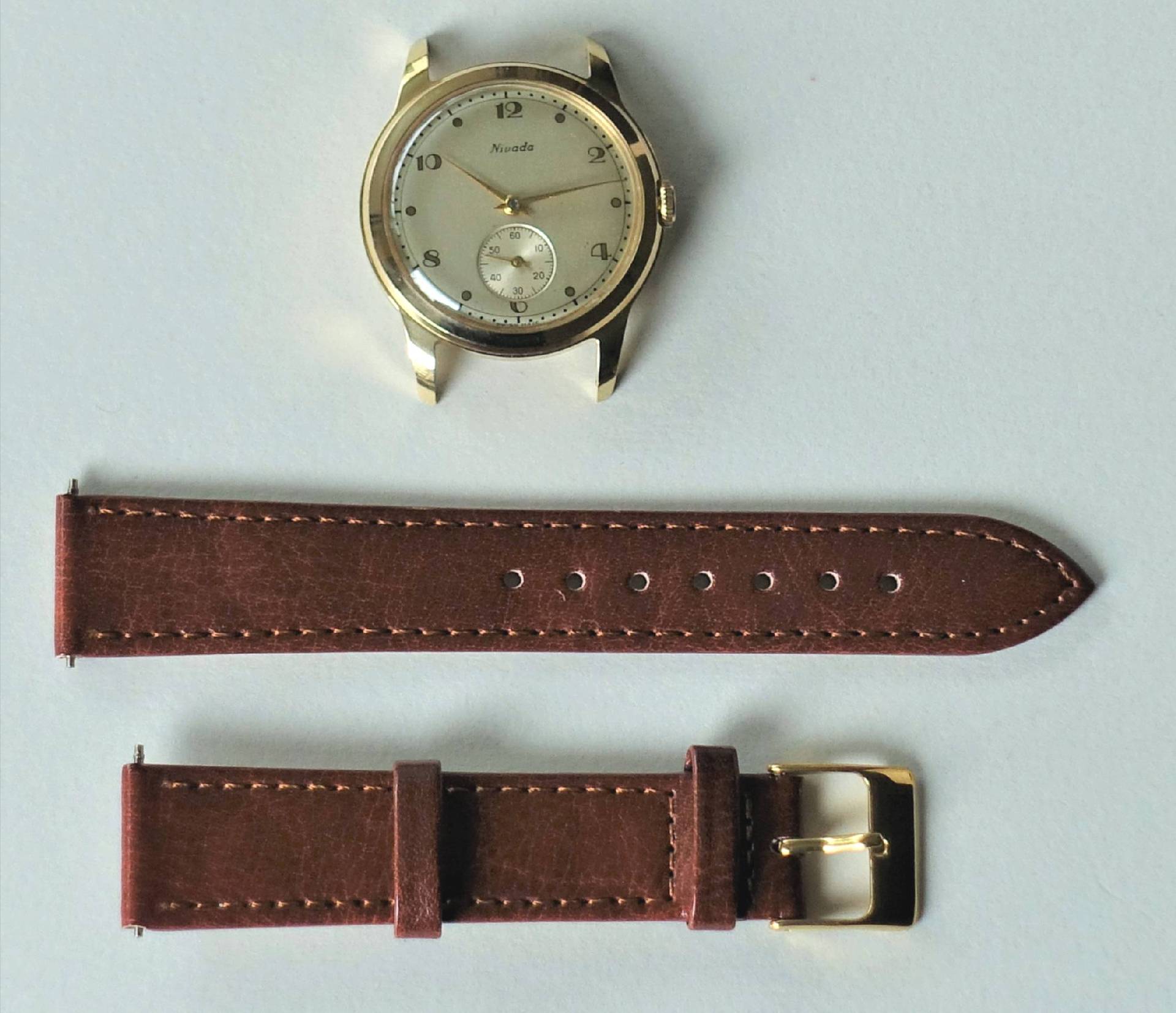 Goldfarbene Armbanduhr mit hellem Zifferblatt und braunem Lederarmband in zwei Teilen.