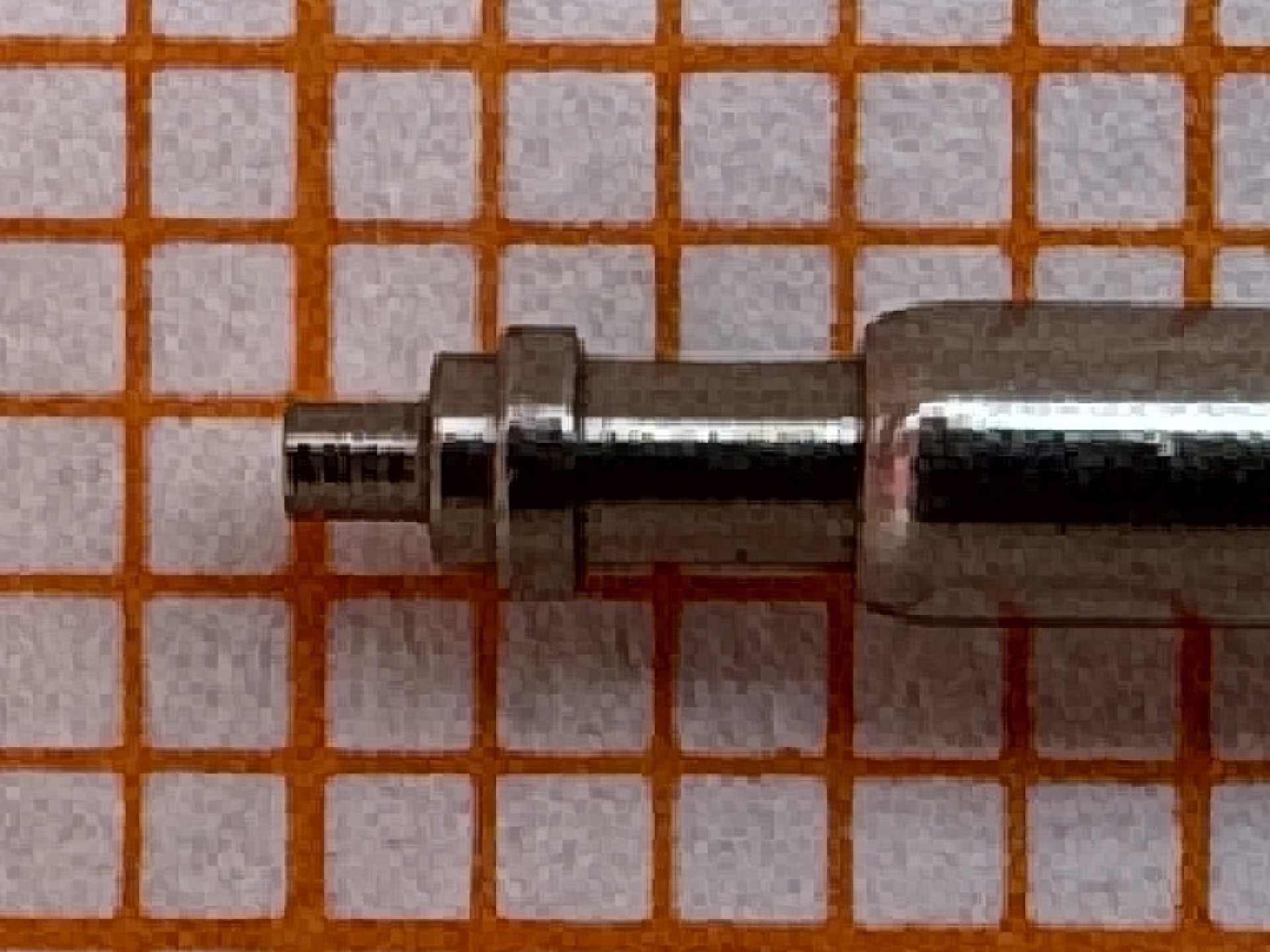 Metallene Aufzugswelle für Armbanduhren, auf kariertem Hintergrund.